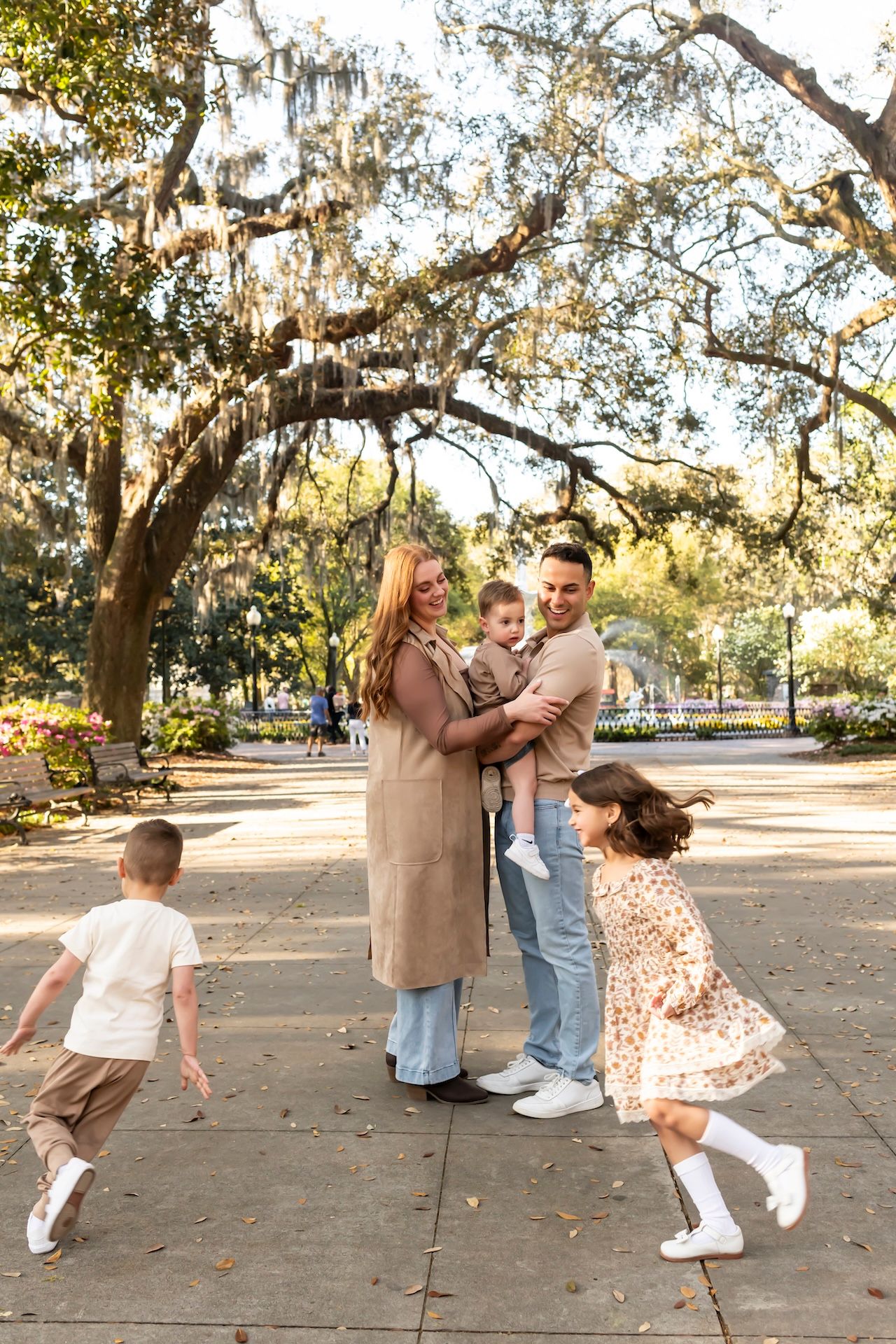 Family enjoying a fun spinning dance moment under moss-draped oak trees in a park.