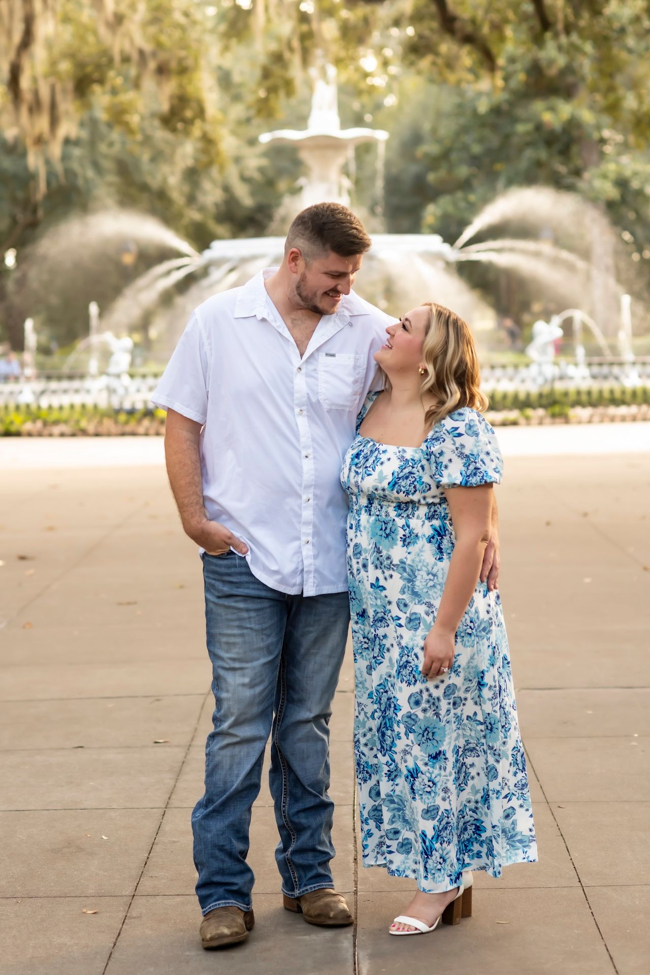 A couple in coordinating outfits share a tender moment in front of a fountain.