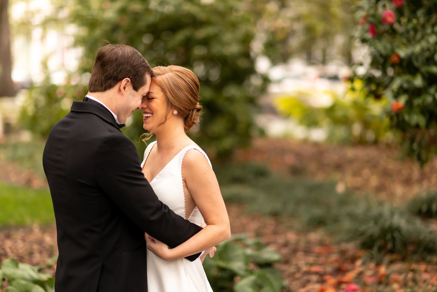 A couple shares an intimate moment together in an outdoor garden setting surrounded by autumn leaves and foliage.