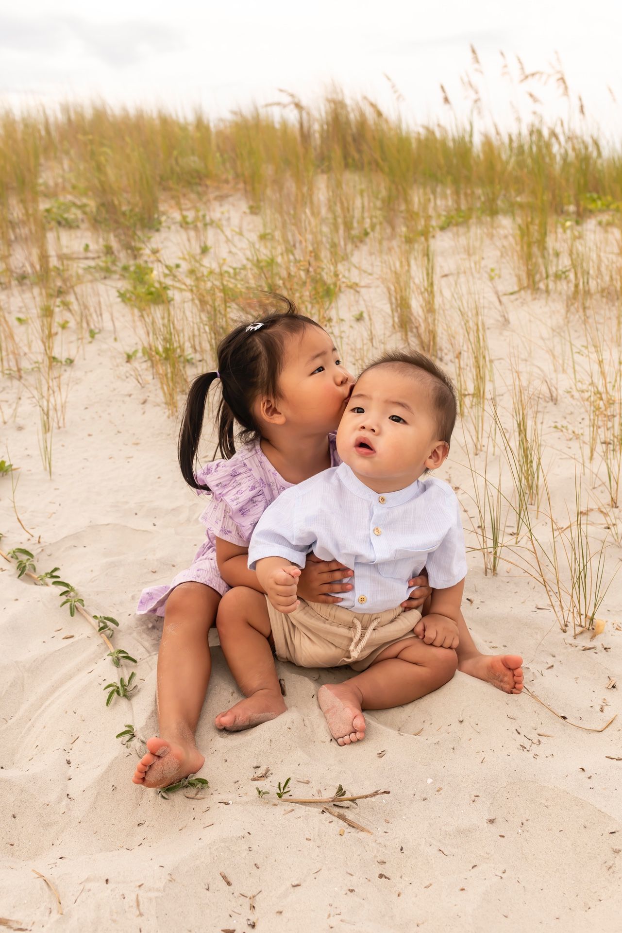 Two children play together on sandy dunes with beach grass growing in the background.