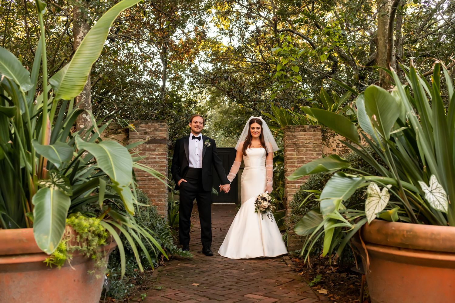 A romantic garden pathway surrounded by lush greenery and terracotta planters creates an intimate wedding venue setting.