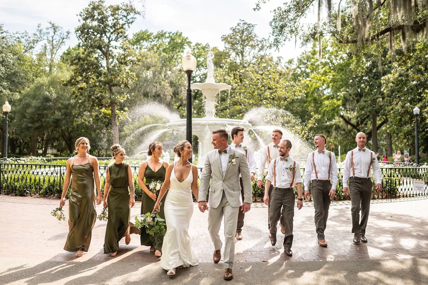 A wedding party walking together on a tree-lined path in Savannah with Spanish moss hanging overhead.