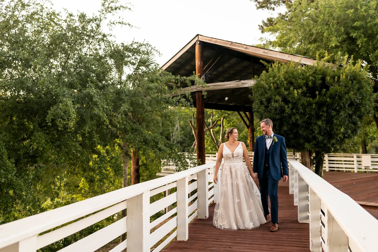 A couple walks together on a wooden bridge under a covered archway surrounded by lush greenery.