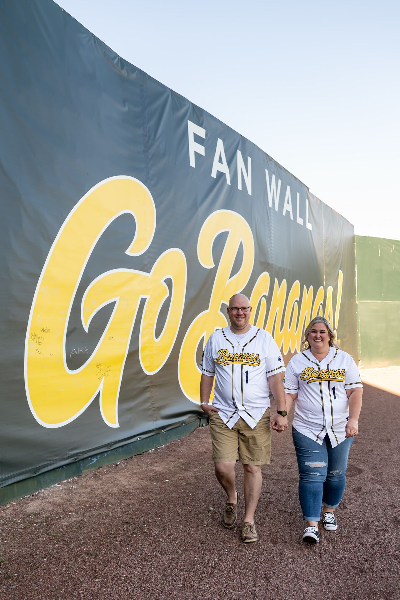 Two people walk along a curved green wall with yellow lettering in an outdoor setting, shown in progressive stages.