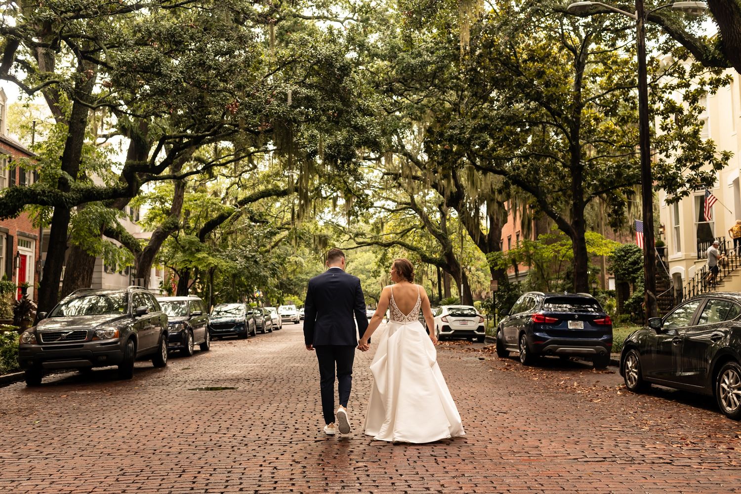 A romantic couple walks down a beautiful tree-lined cobblestone street in Savannah, Georgia on their wedding day.