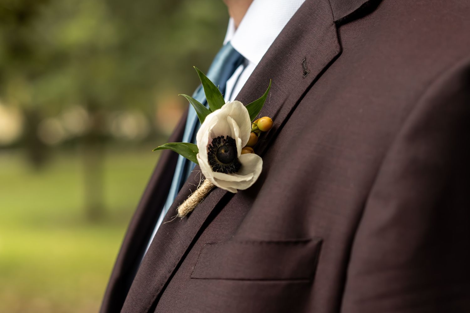 A groom in a dark suit jacket shows the front then the back featuring intricate pearl details and gold embellishments.