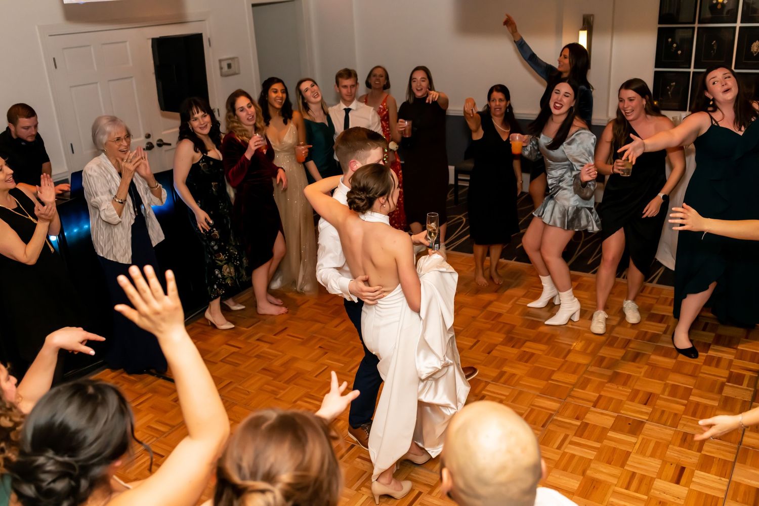 Wedding guests dancing enthusiastically on a parquet dance floor during a lively reception celebration.