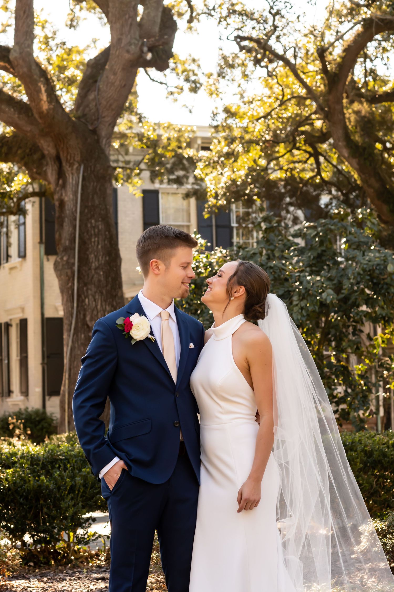 A wedding couple shares an intimate moment under oak trees draped in golden sunlight at their outdoor celebration.