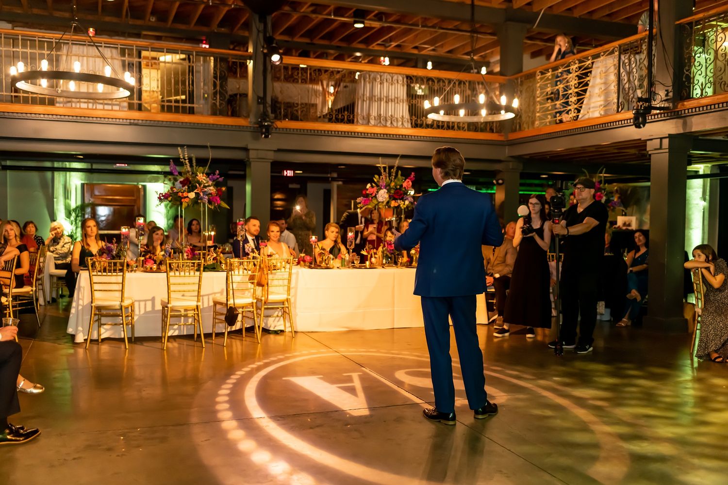 Panoramic view of a dimly lit indoor venue with warm lighting and exposed wooden beams showing people gathering.