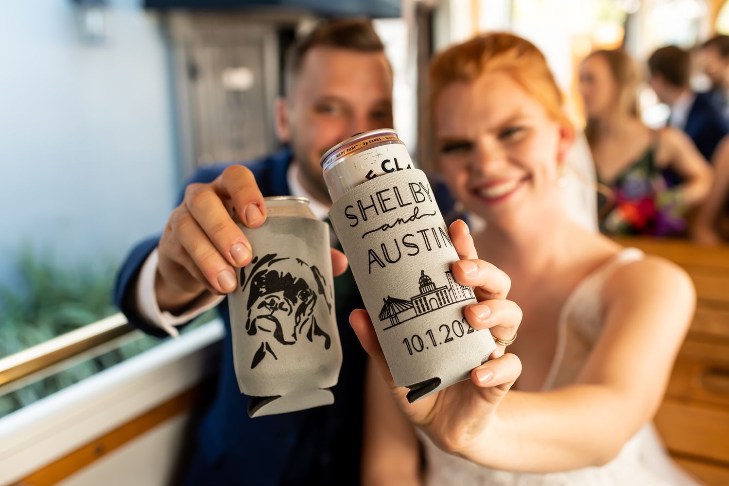 Two people holding up custom printed beer cans with illustrations while smiling at a bar.