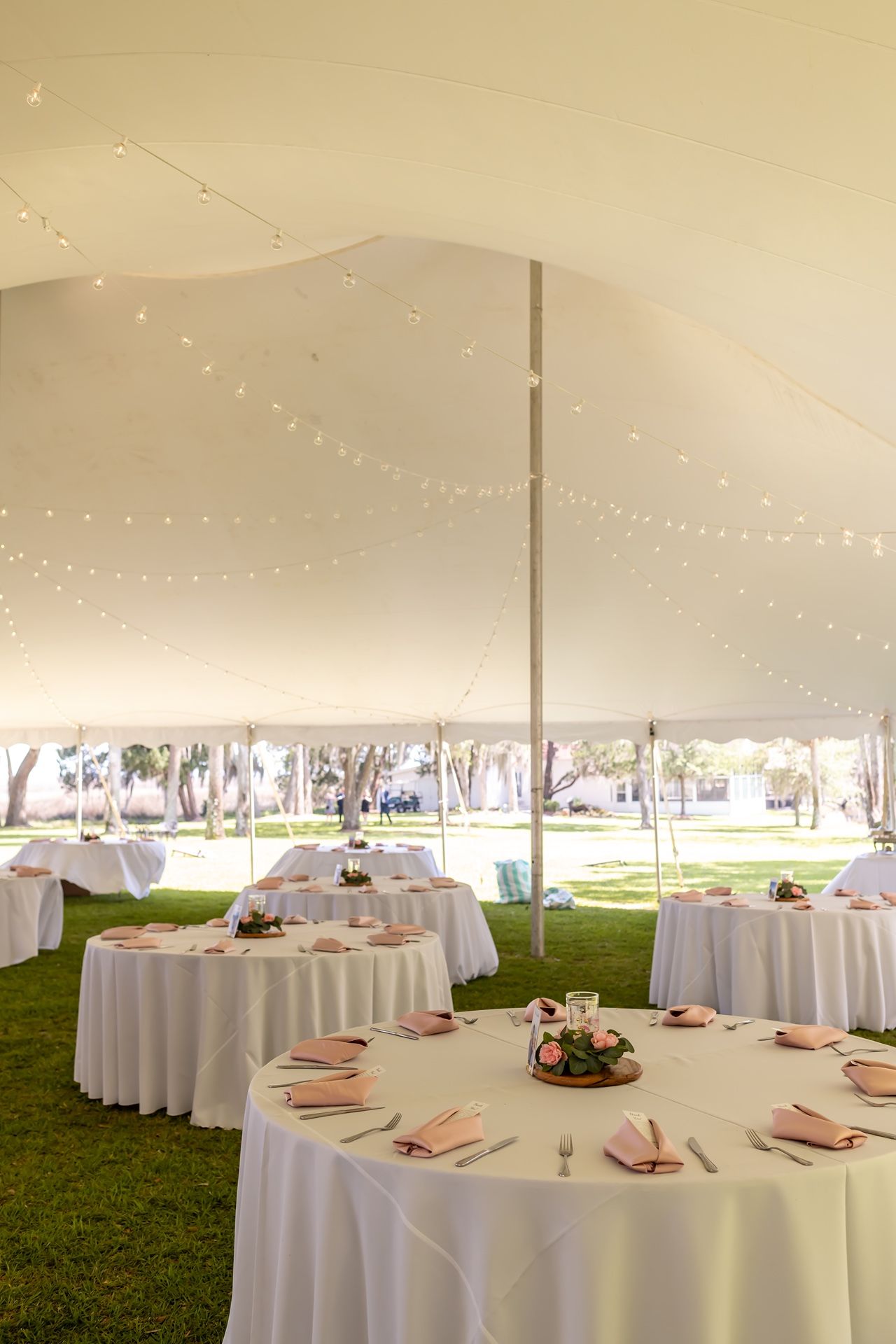 Elegant wedding tent reception space with round white-clothed tables and string lights creating a romantic atmosphere.