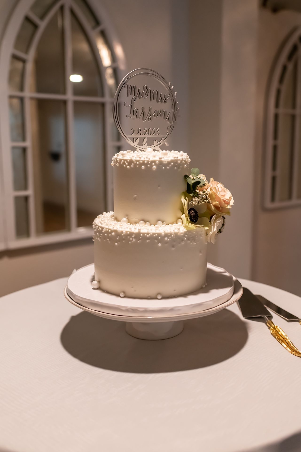 Wedding cake display closeup sequence showing a modern white cake with floral accents on a simple stand with fairy lights.