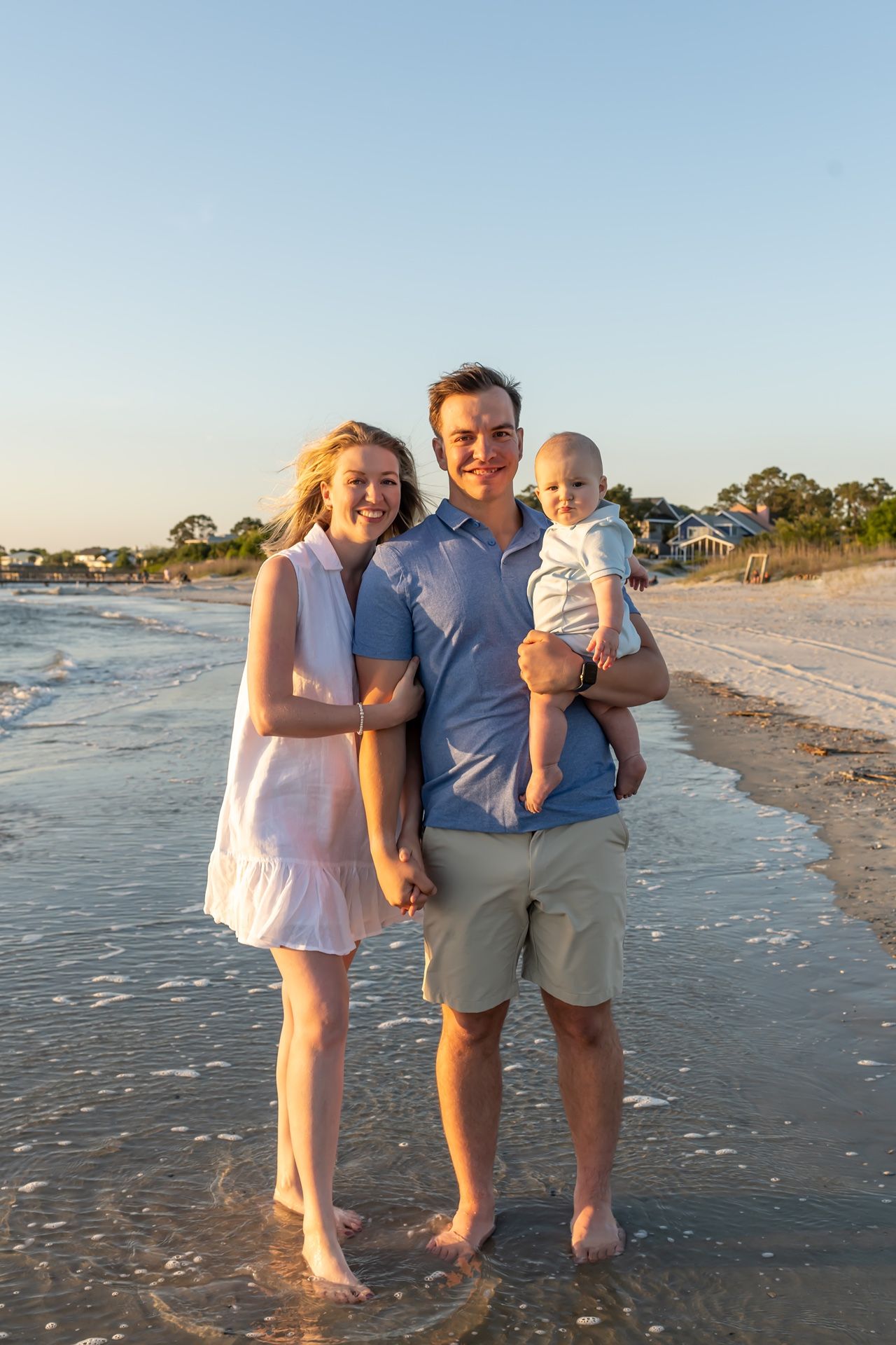 Family enjoying sunset together on a sandy beach while standing in shallow ocean water at golden hour.