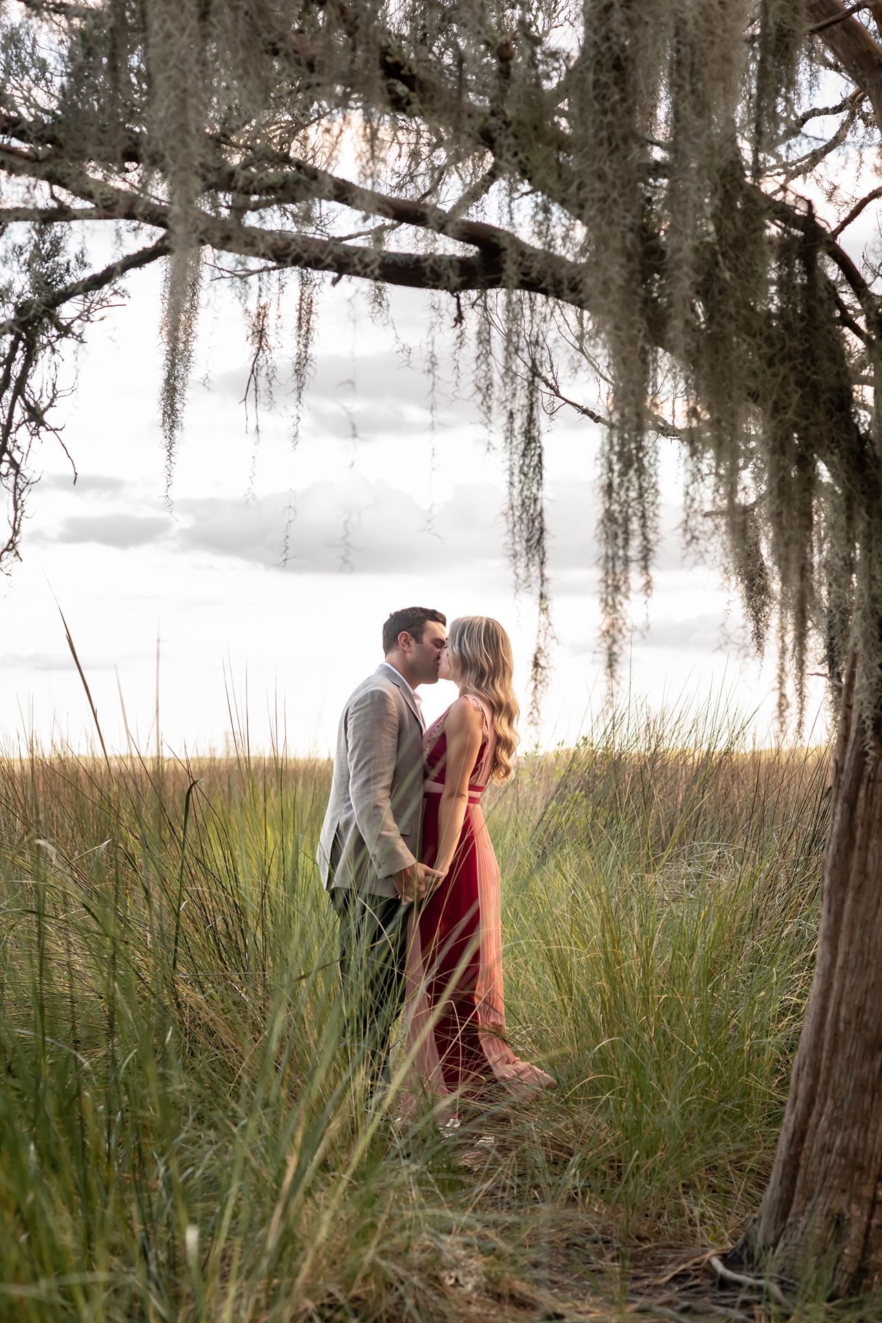 A romantic moment captured between two people among tall marsh grass and moss-covered trees.