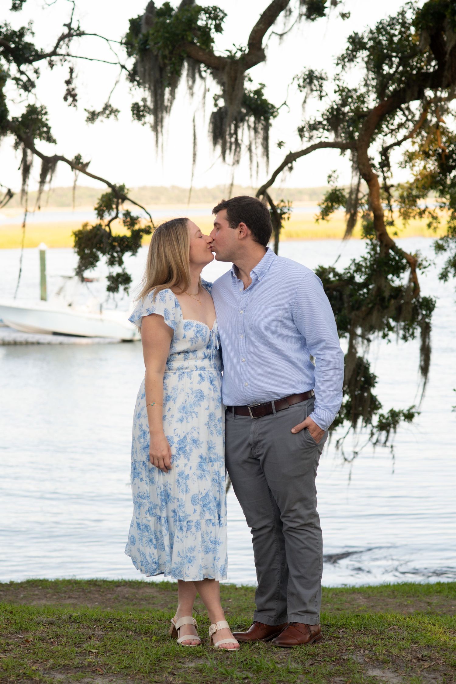 A couple shares romantic moments by a lakeside at sunset with Spanish moss hanging from trees in the background.