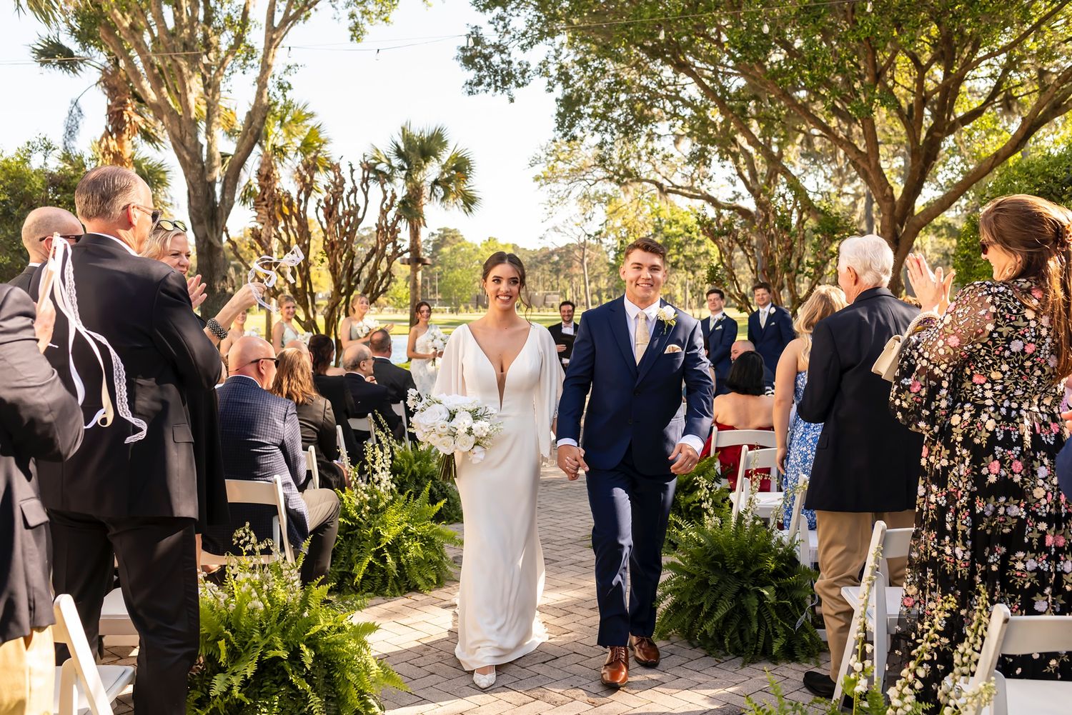 Wedding celebration along a scenic outdoor venue with guests gathering under palm trees at golden hour.