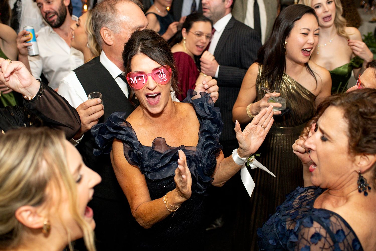Wedding guests dancing and laughing together on a crowded dance floor during a lively reception celebration.