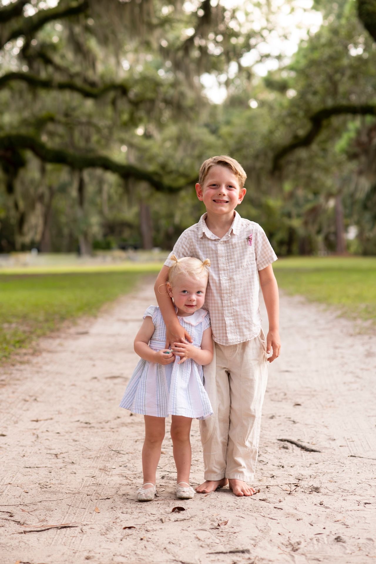 Two young siblings pose on a sandy path under moss-draped oak trees at Six Oaks in Sea Pines.