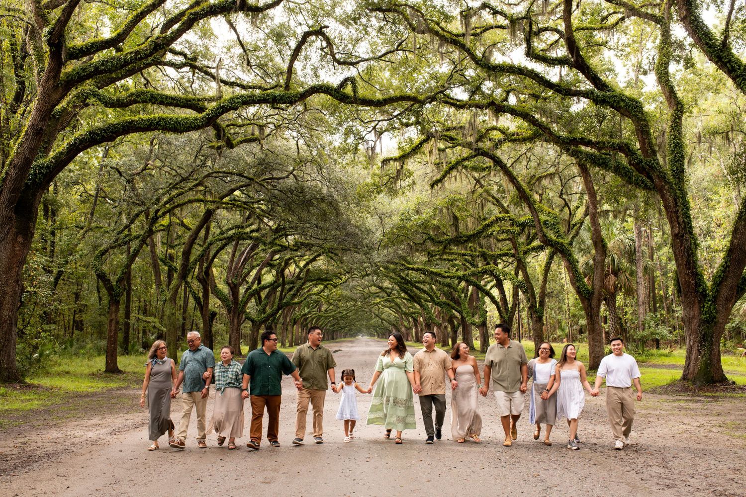Large family group walking together on a scenic tree-lined path canopied by sprawling oak trees.