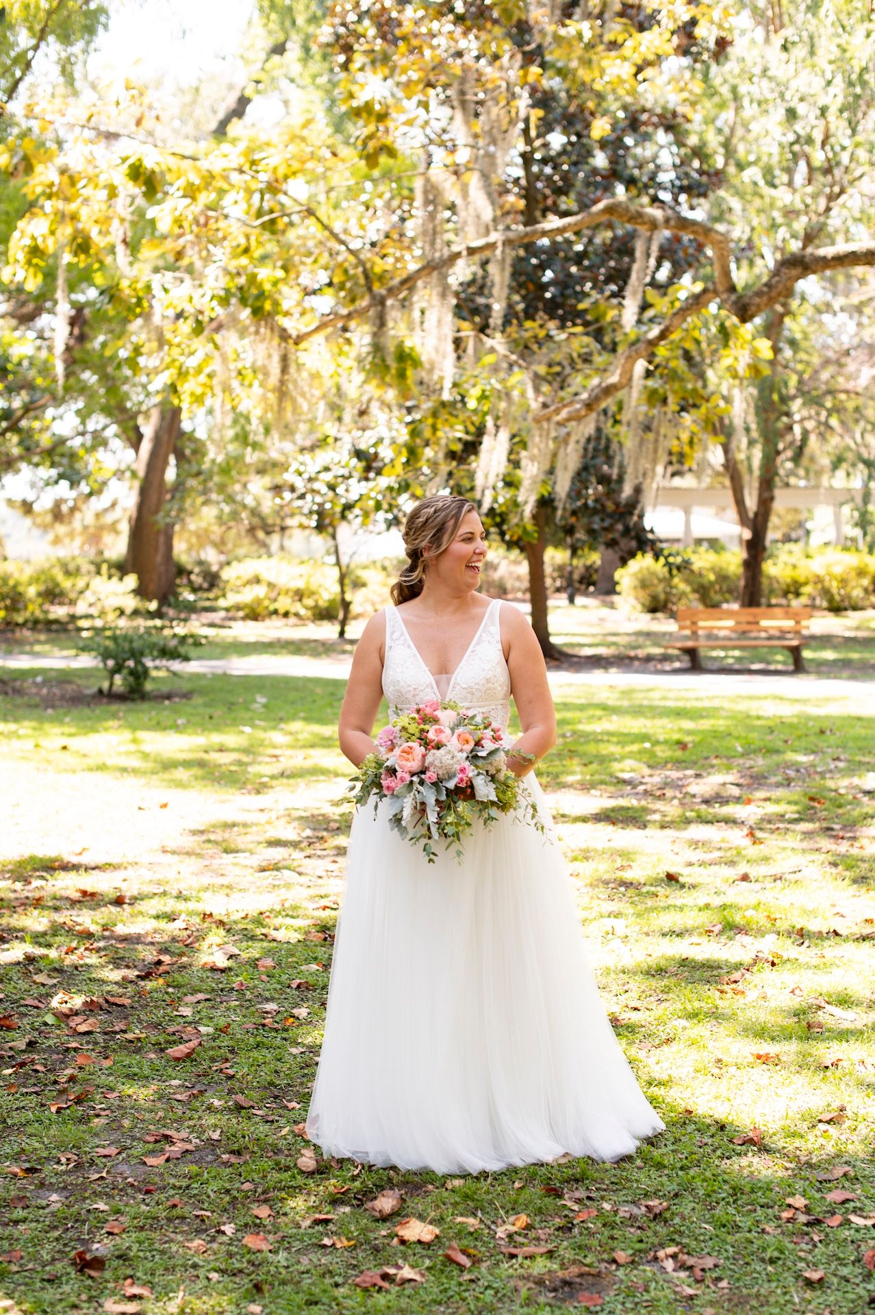 A bride in a white wedding dress stands in a sunlit outdoor garden in Forsyth Park in Savannah, Georgia.