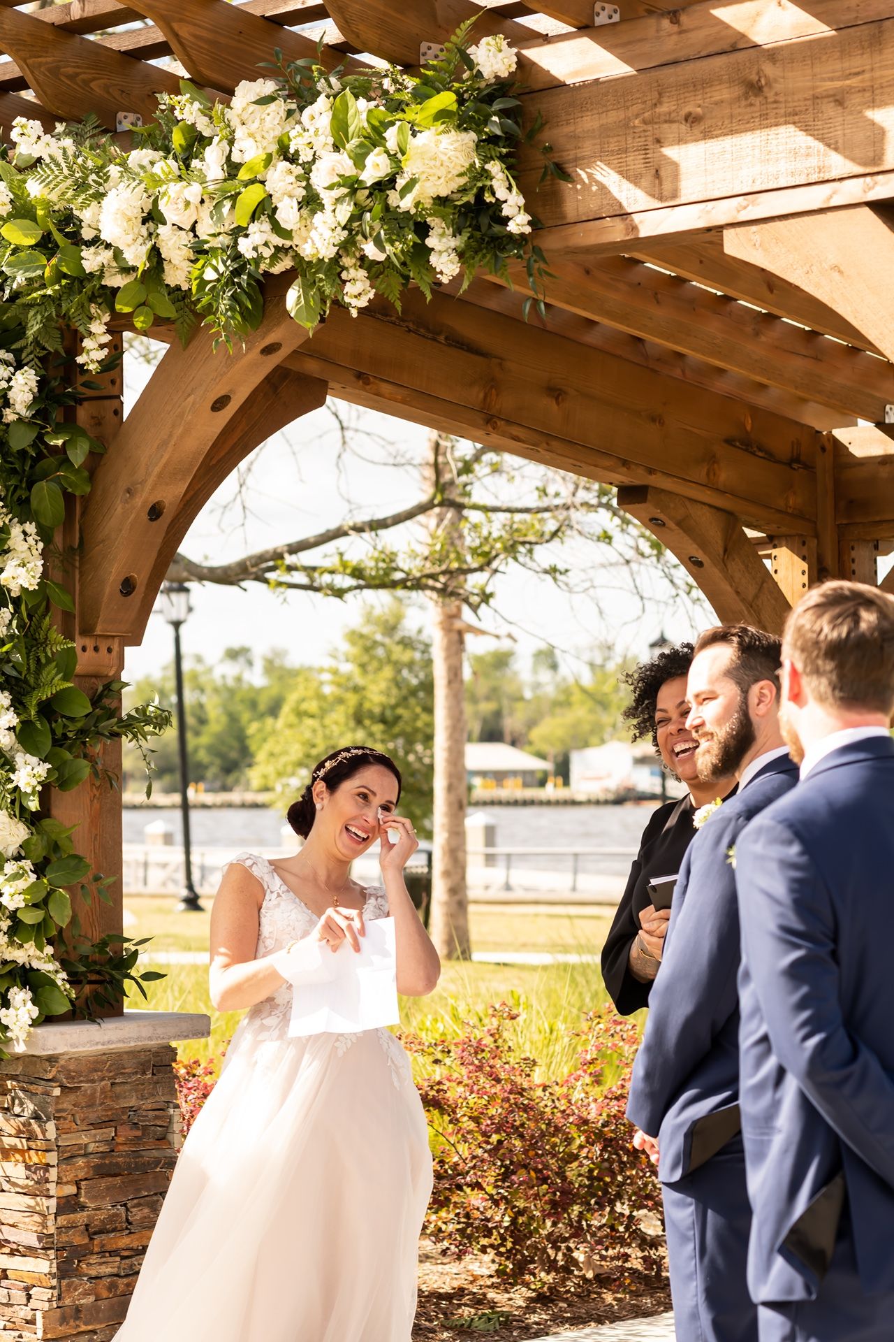 A beautiful outdoor wedding ceremony setup with a wooden pergola decorated with white floral arrangements and greenery.