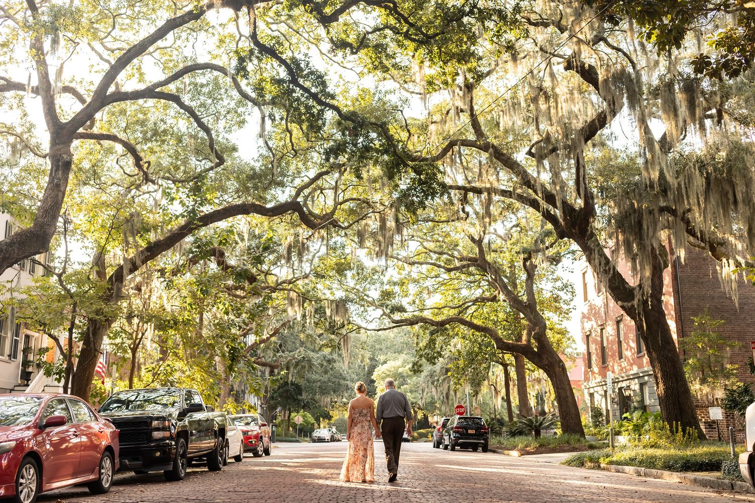 A couple stands beneath majestic live oak trees draped with Spanish moss on a charming Savannah city street.