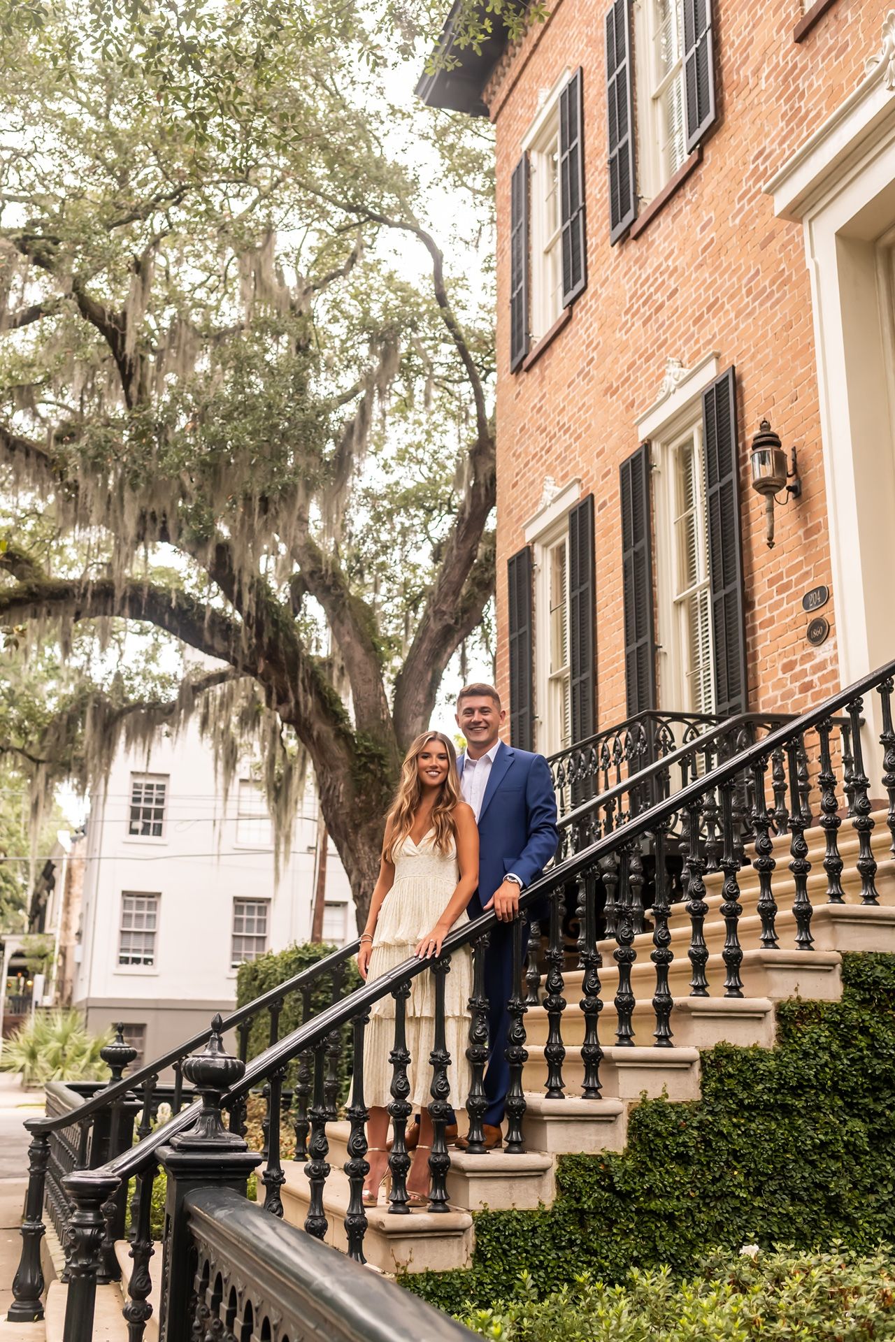 Historic brick townhouse with wrought iron railings and Spanish moss draped oak trees creating a romantic Southern atmosphere.