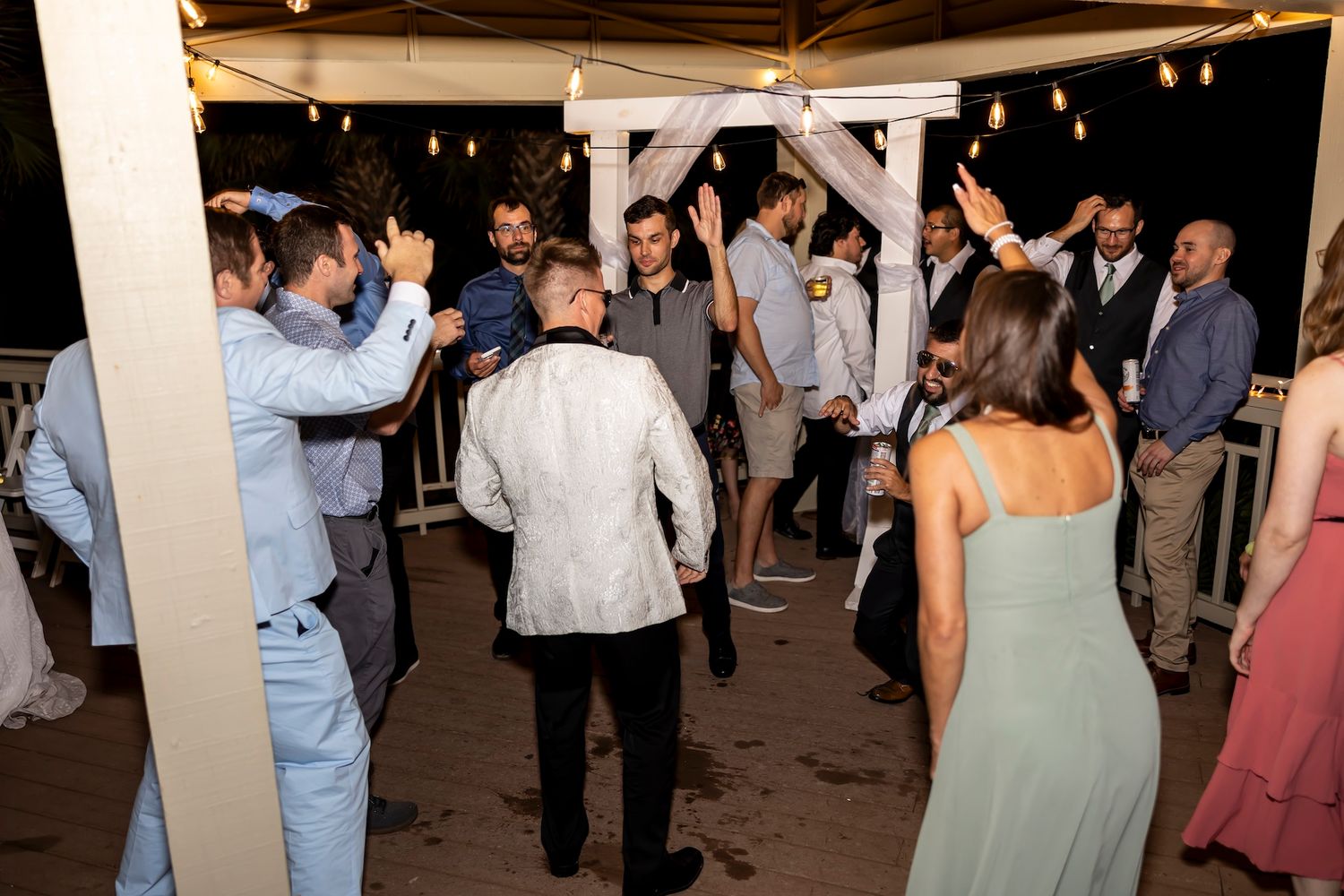 Wedding guests dance and celebrate on a dimly lit dance floor at an evening reception.