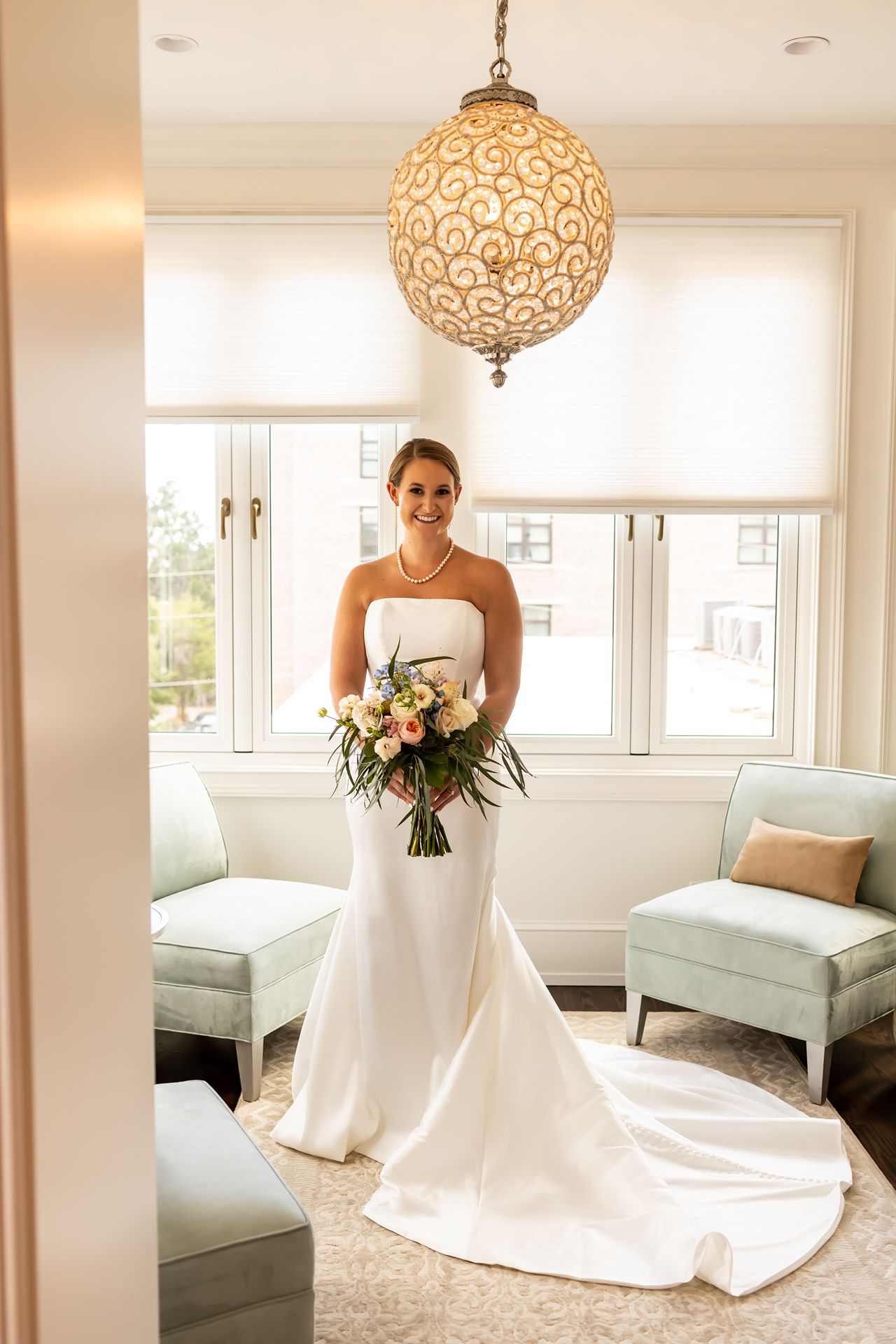 Elegant white wedding gown with train captured in bright room with decorative globe pendant light and mint seating.