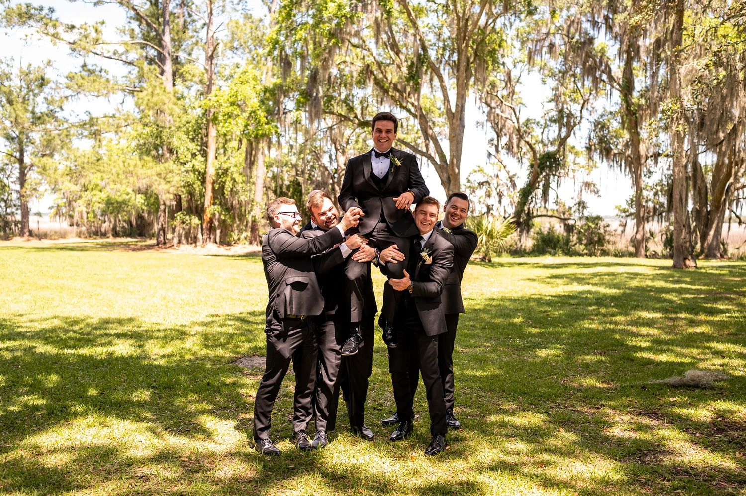 A formal group poses together on a sunny lawn with Spanish moss draped trees in the background.