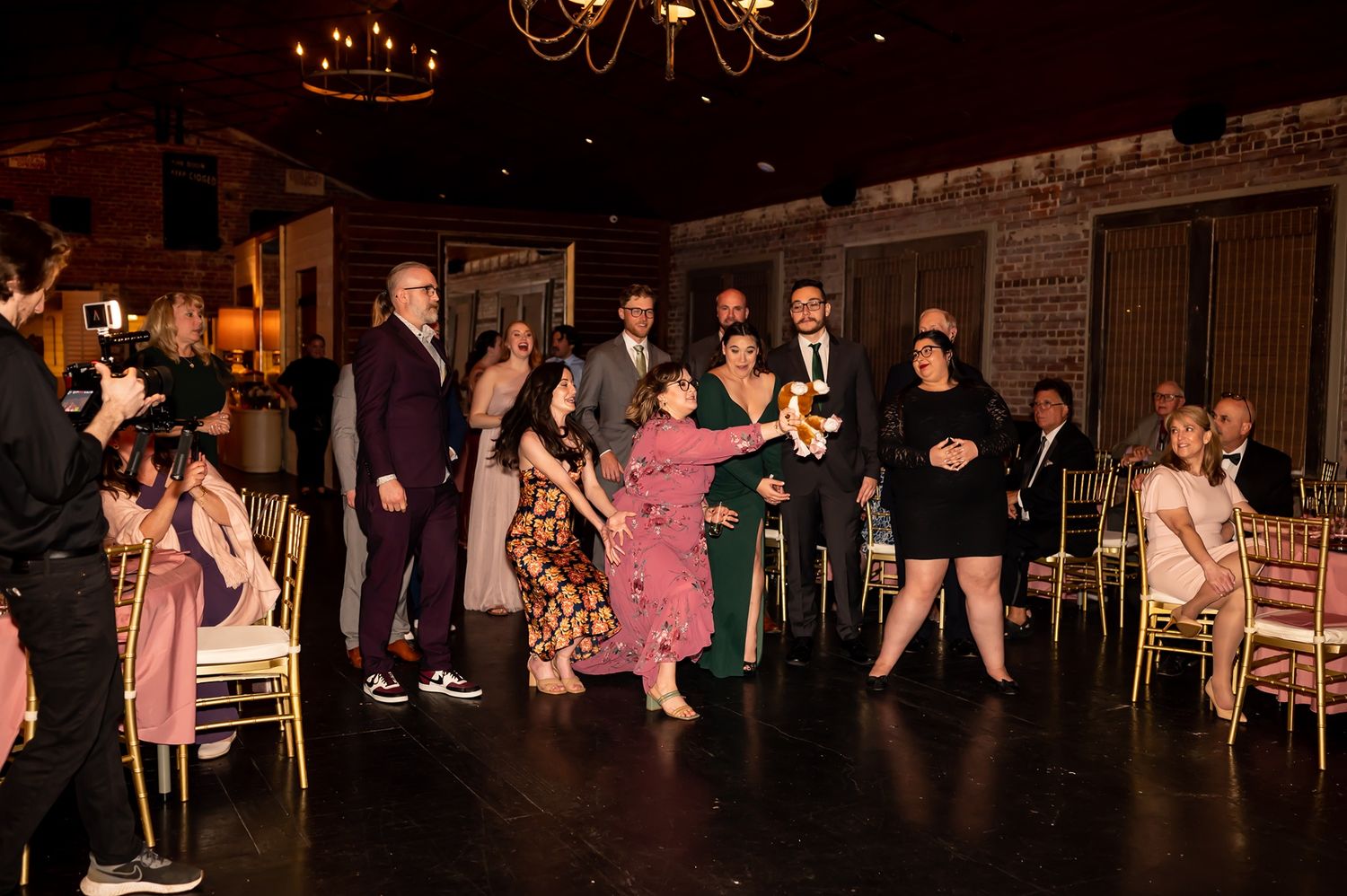 Wedding guests dance and celebrate on dimly lit dance floor during evening reception.