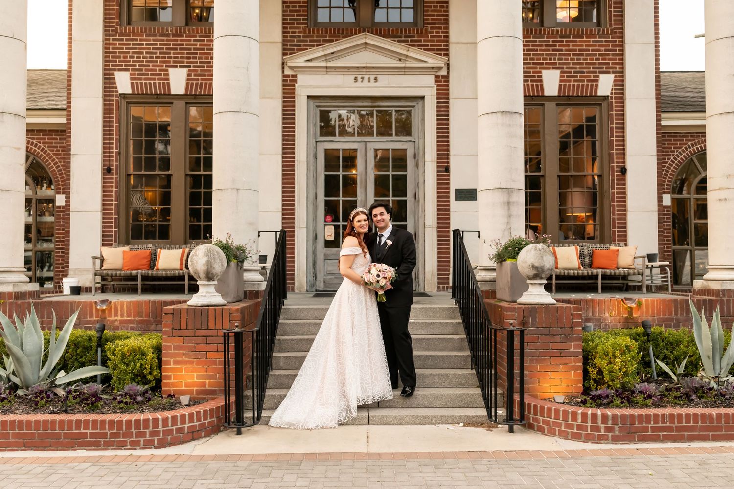A bride and groom standing along a grand brick building with large white columns.