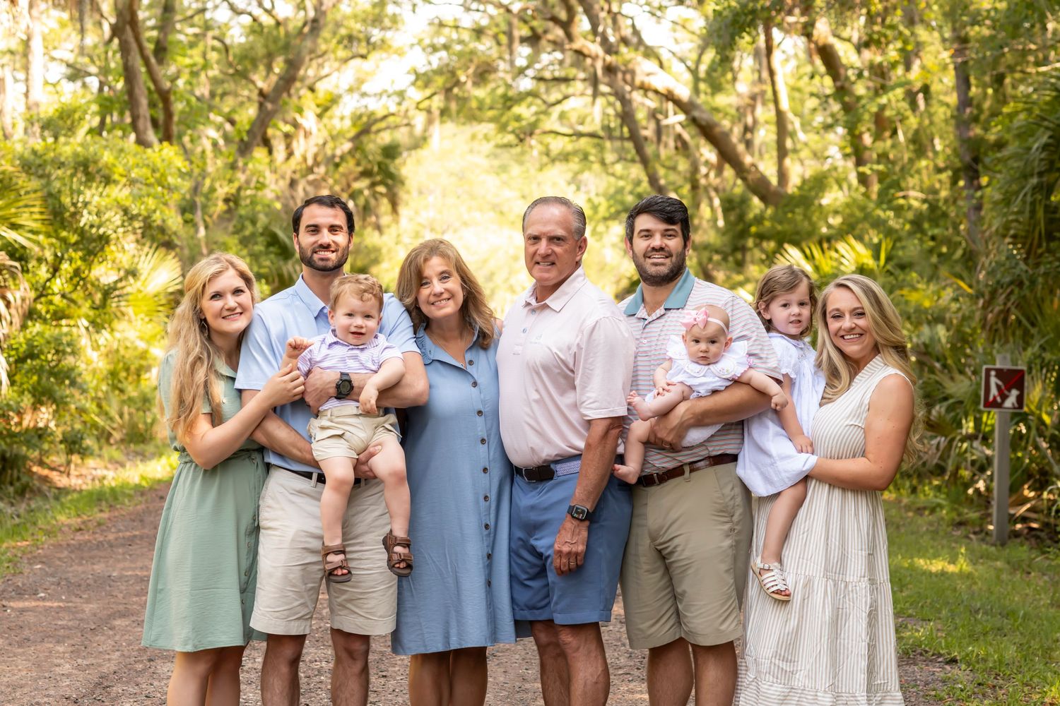 Family group poses together on a wooded path during outdoor photo session in natural setting with sunlit background.