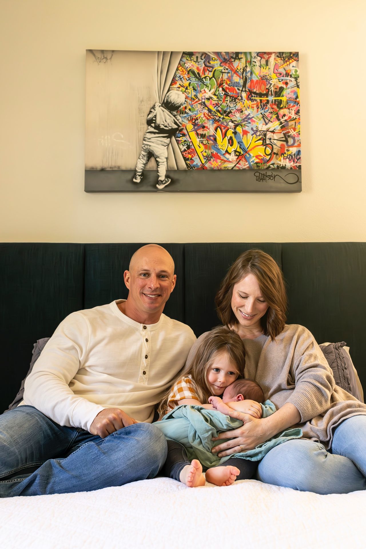Group cuddles together on a comfortable bed under colorful wall art during a relaxing moment at home.