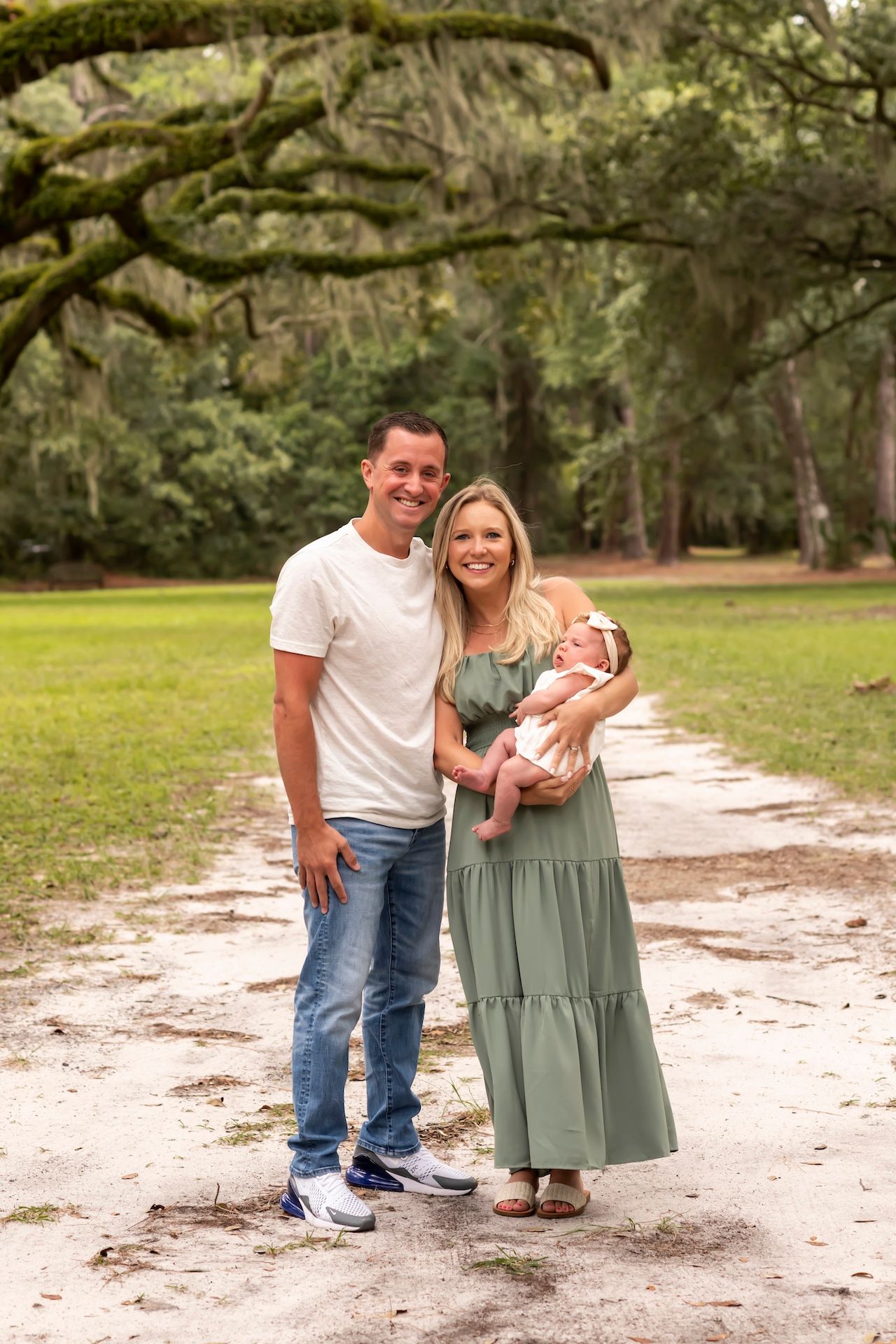 A couple poses together in a casual outdoor setting on a sandy pathway surrounded by trees.