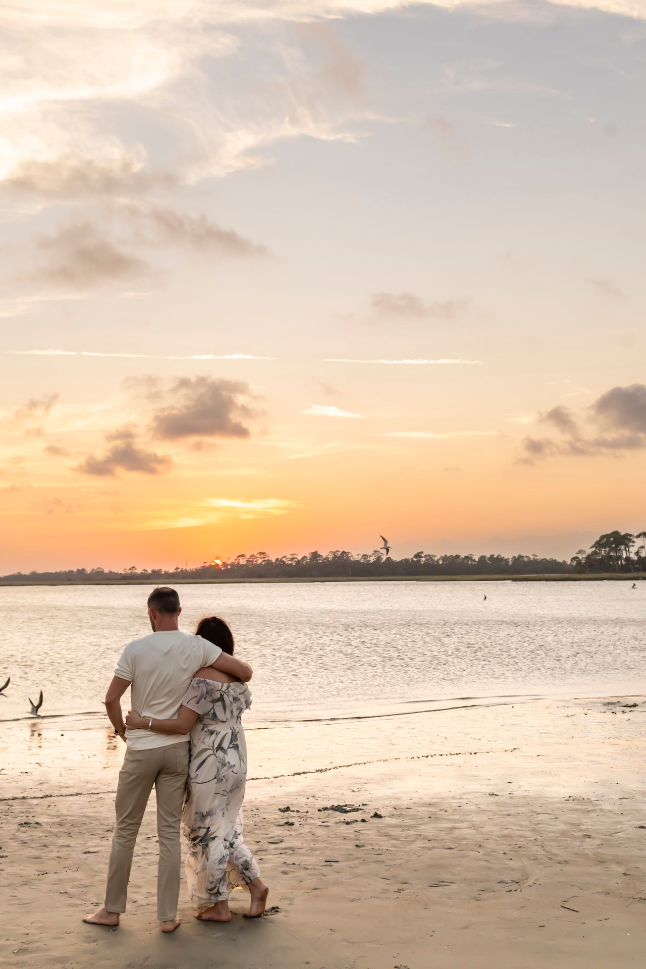 Silhouetted couple enjoying a romantic moment on a tropical beach at sunset with palm trees in distance.