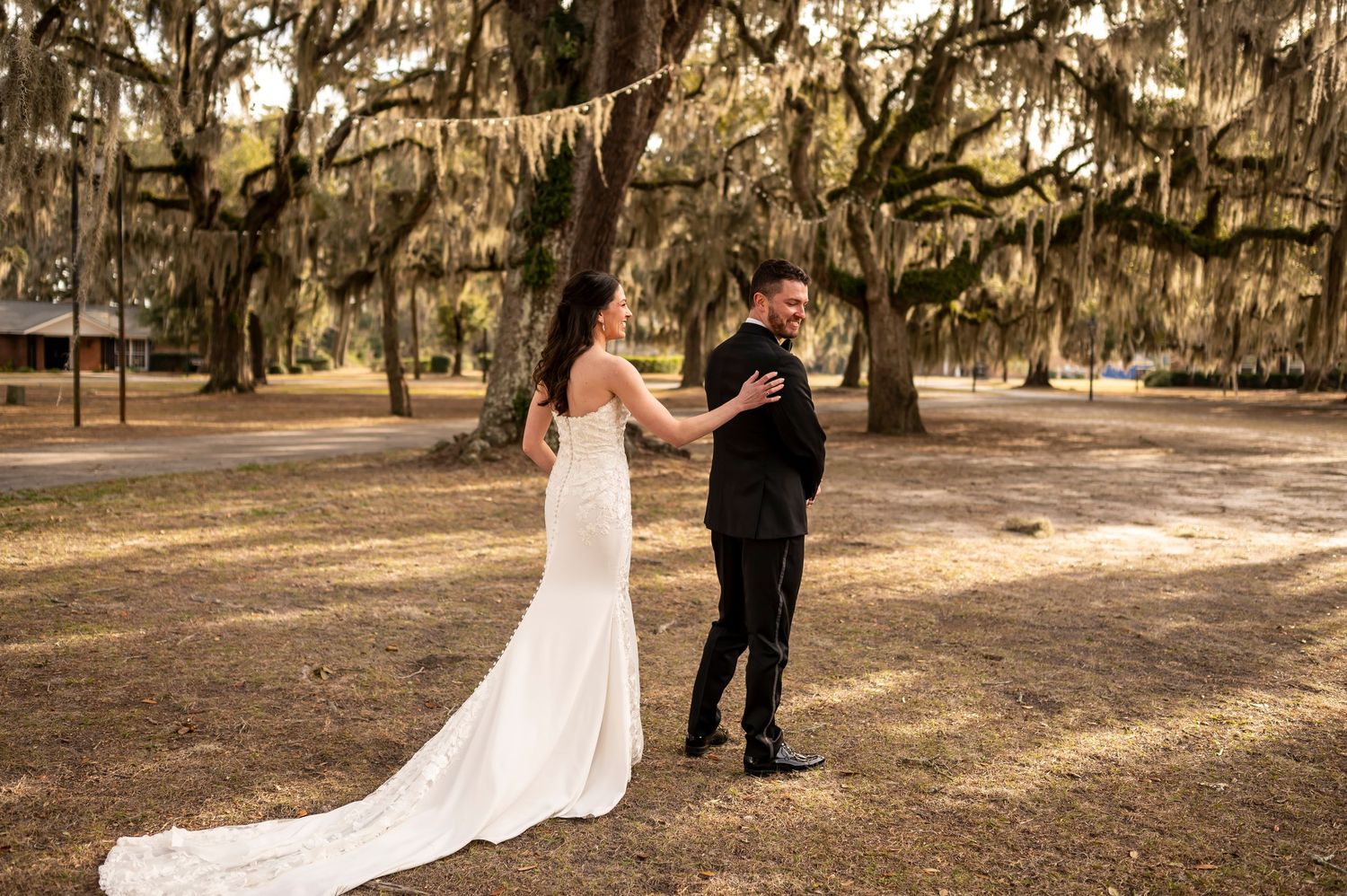 A bride and groom share a tender moment in a garden setting with oak trees draped in Spanish moss.