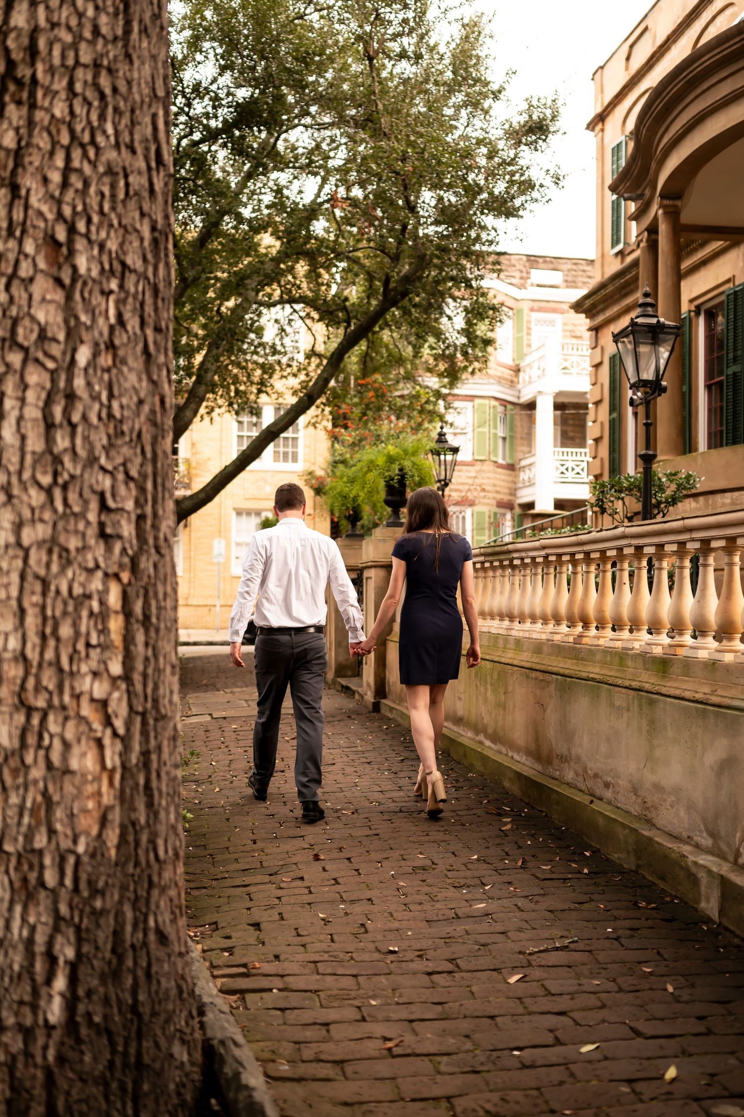 A couple walking together down a historic cobblestone pathway bordered by stone balustrades in warm sunlight.