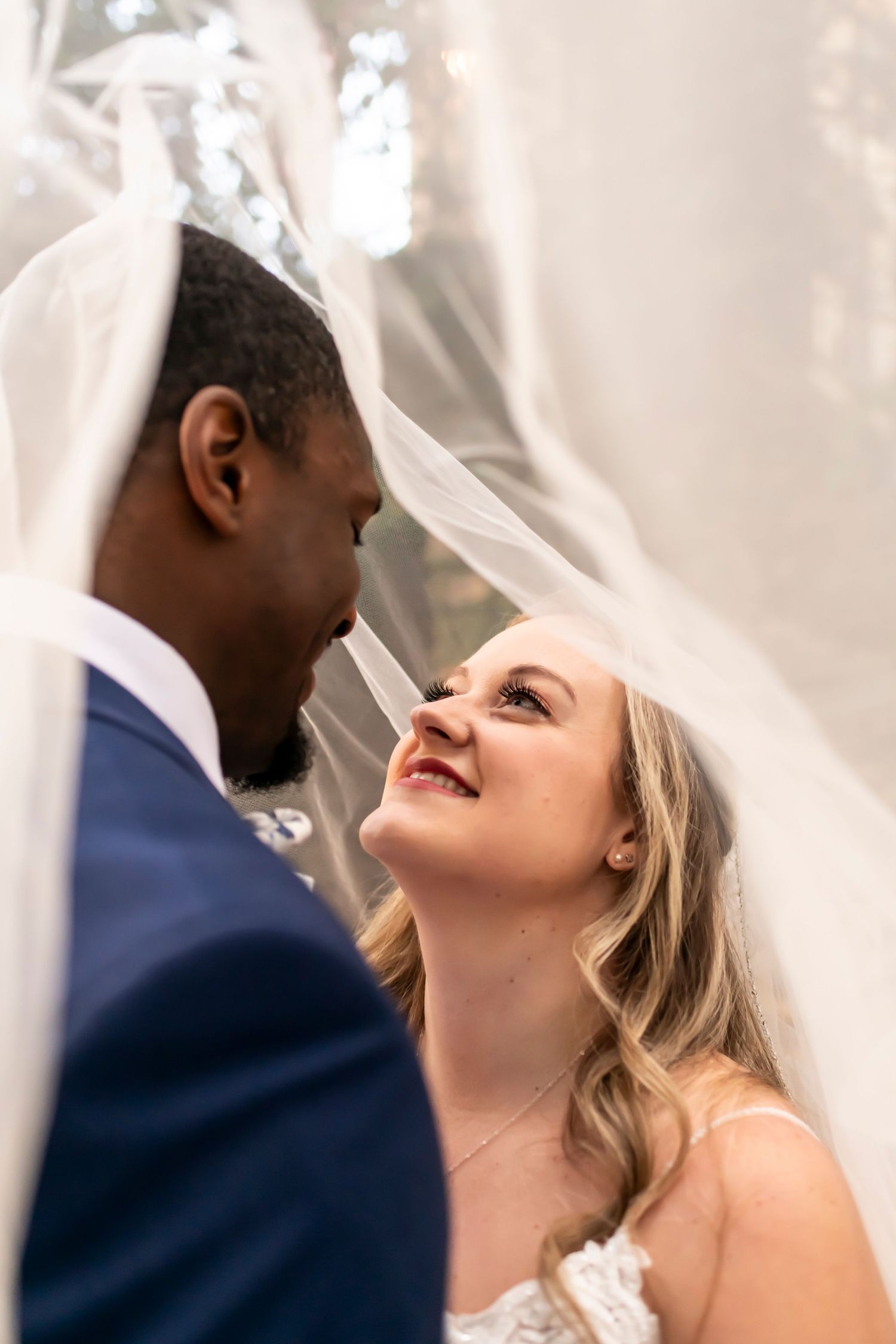 A couple shares a joyful moment on their wedding day, surrounded by white fabric and natural light.