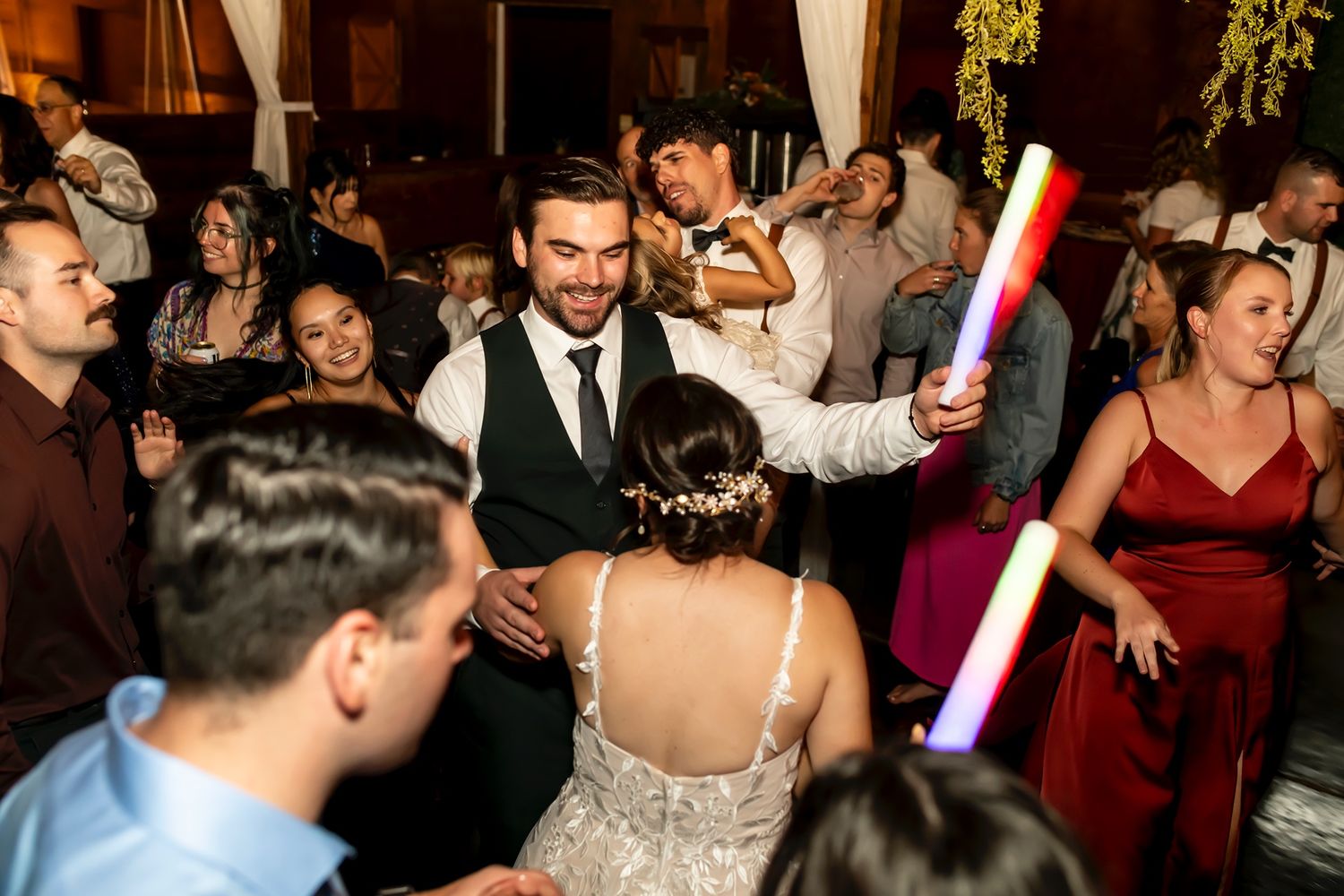 Wedding guests dancing and celebrating at a lively reception with light-up party favors on a crowded dance floor.