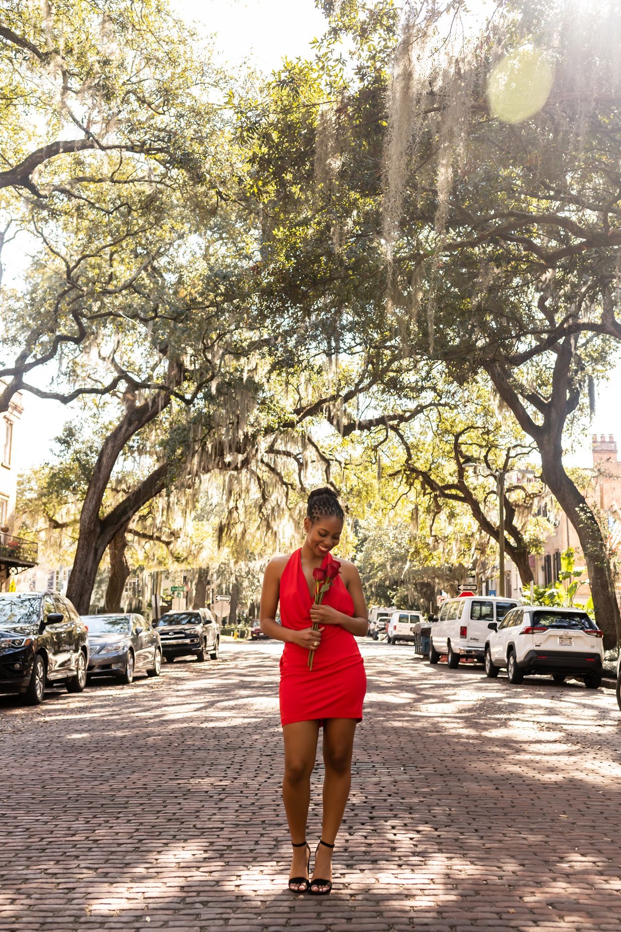 A person in a red dress stands on a brick street lined with Spanish moss-draped oak trees in Savannah.