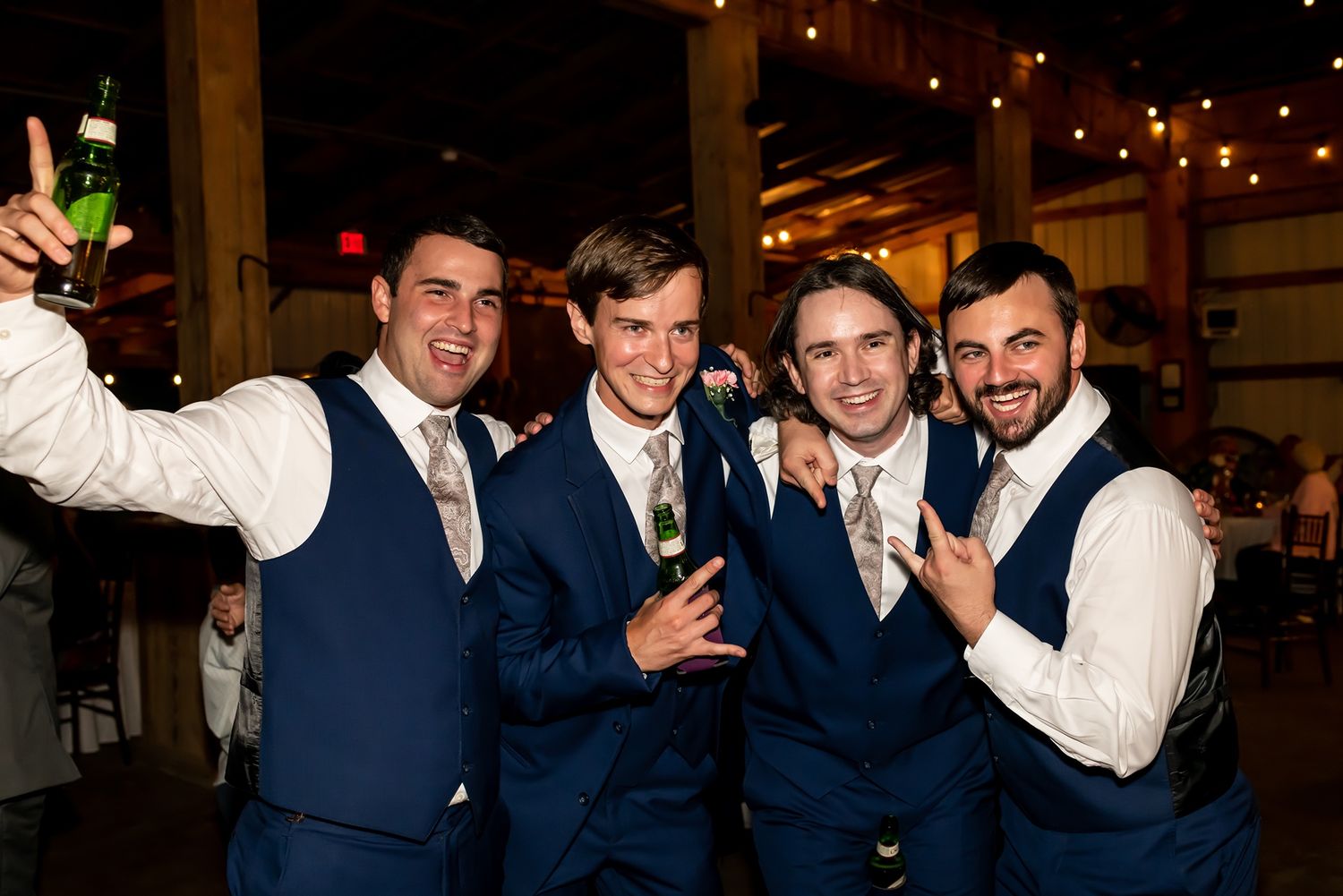 Four groomsmen celebrating at a wedding reception venue with drinks and smiles.