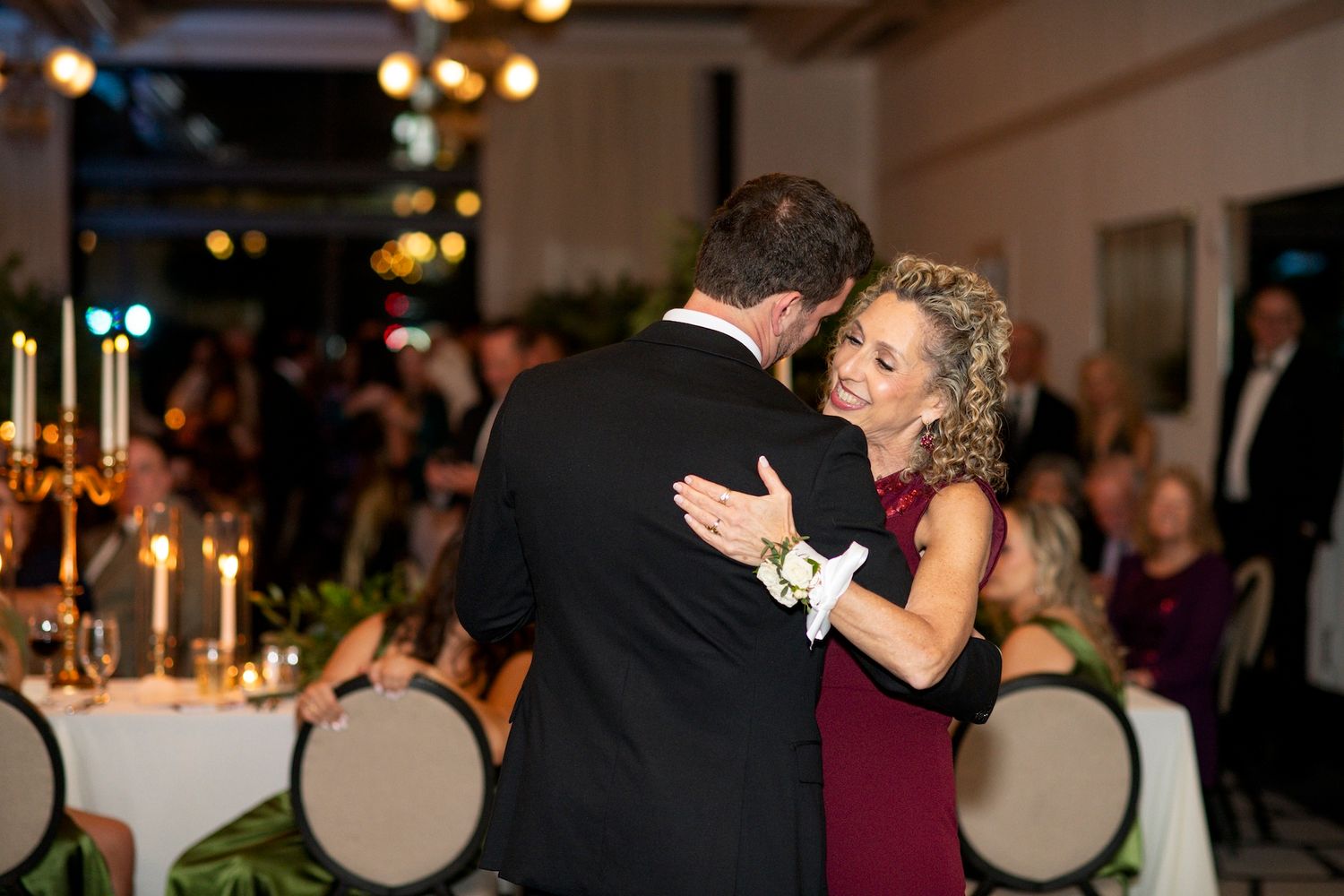 A couple shares a romantic dance at an elegant candlelit reception with guests looking on in the background.