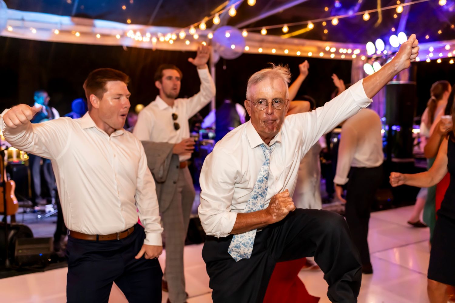 People dancing and having fun at a lively party celebration with string lights and colorful decorations in the background.