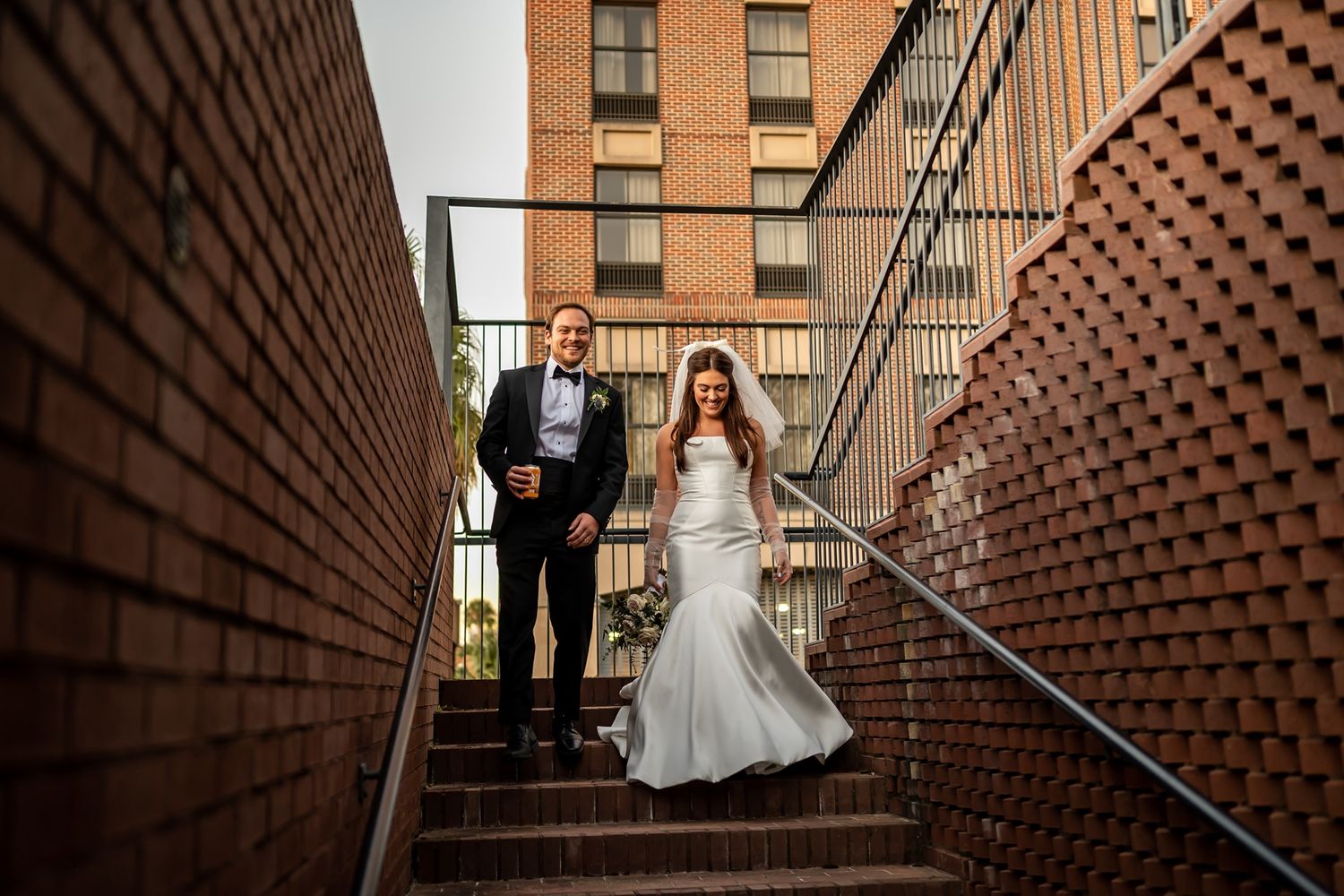 A couple descending brick stairs surrounded by red brick walls and handrails at their wedding ceremony.