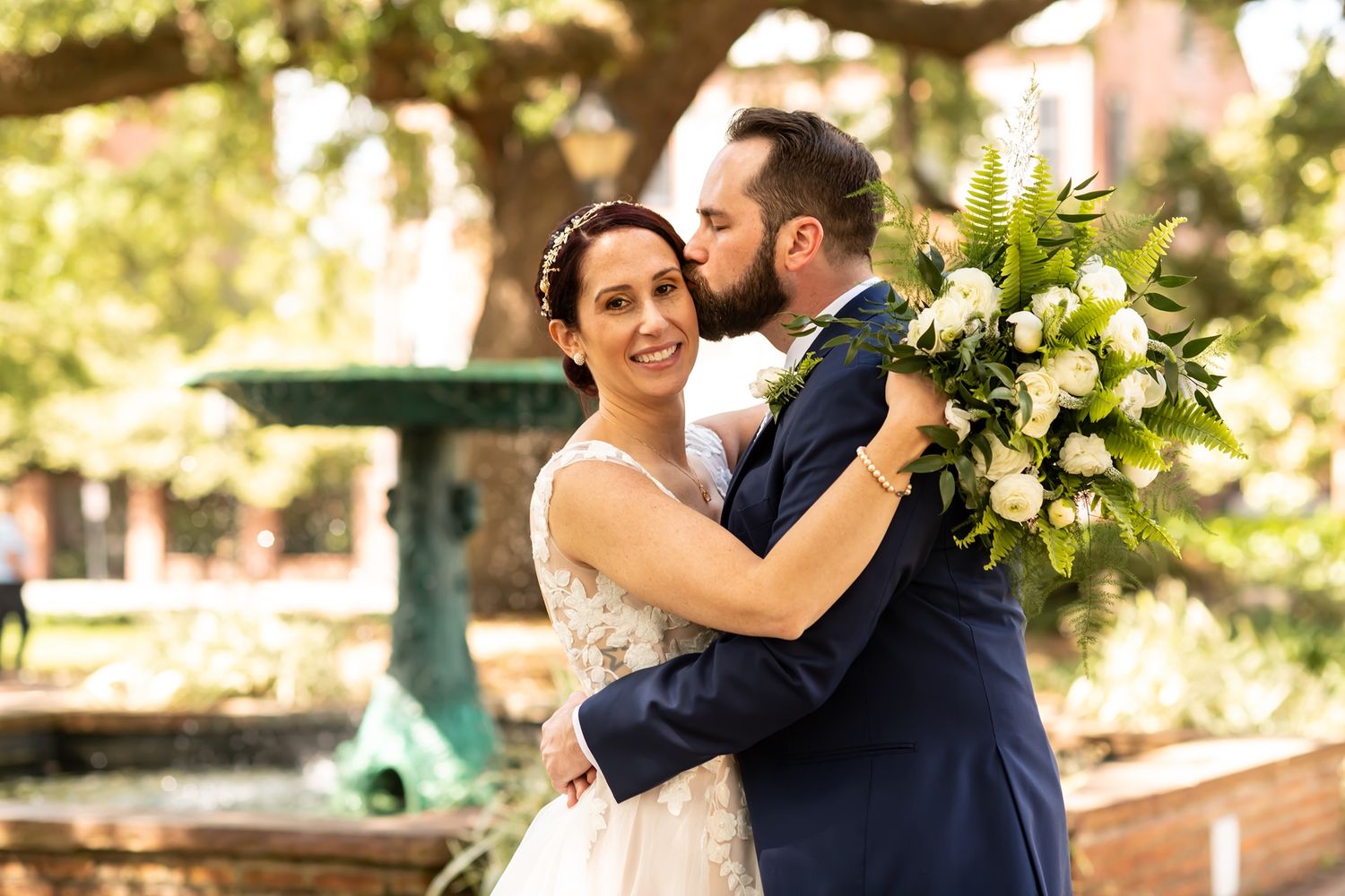 A joyful moment shared between newlyweds embracing outdoors with a beautiful white floral bouquet in sunlit setting.