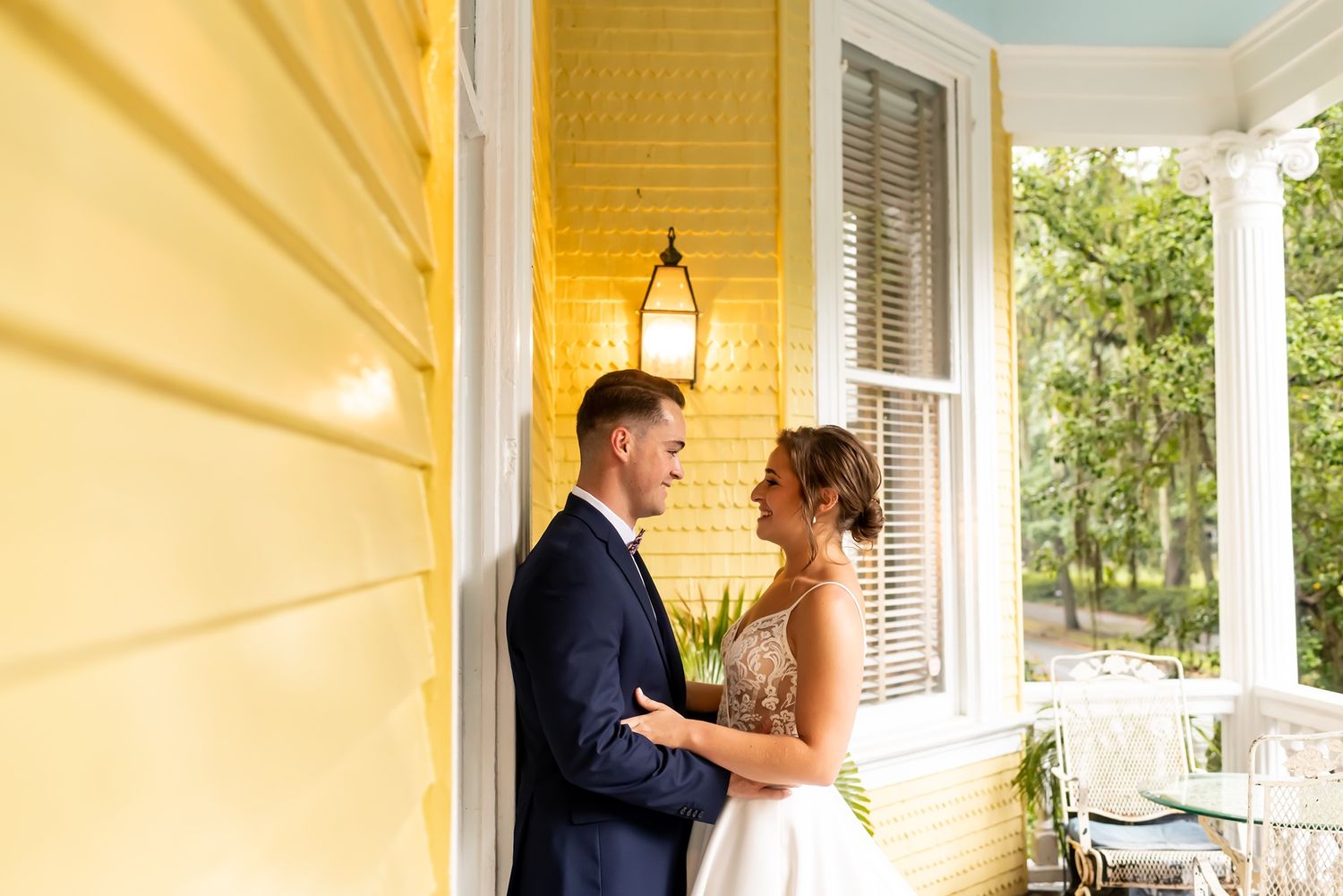 A couple shares an intimate moment together on a sunny porch with yellow walls and white columns.