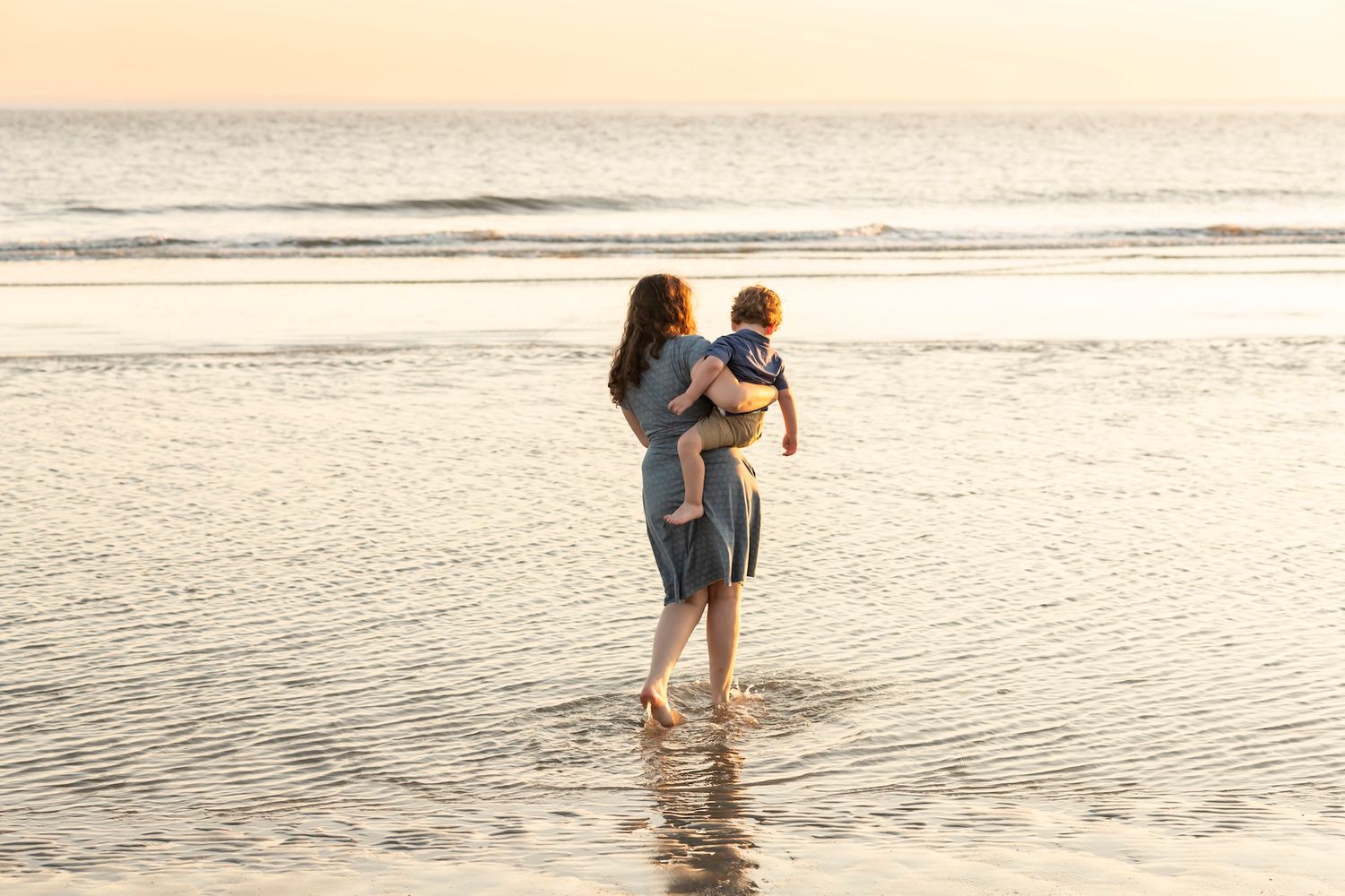 People walking along a serene beach shoreline during golden hour with gentle waves.