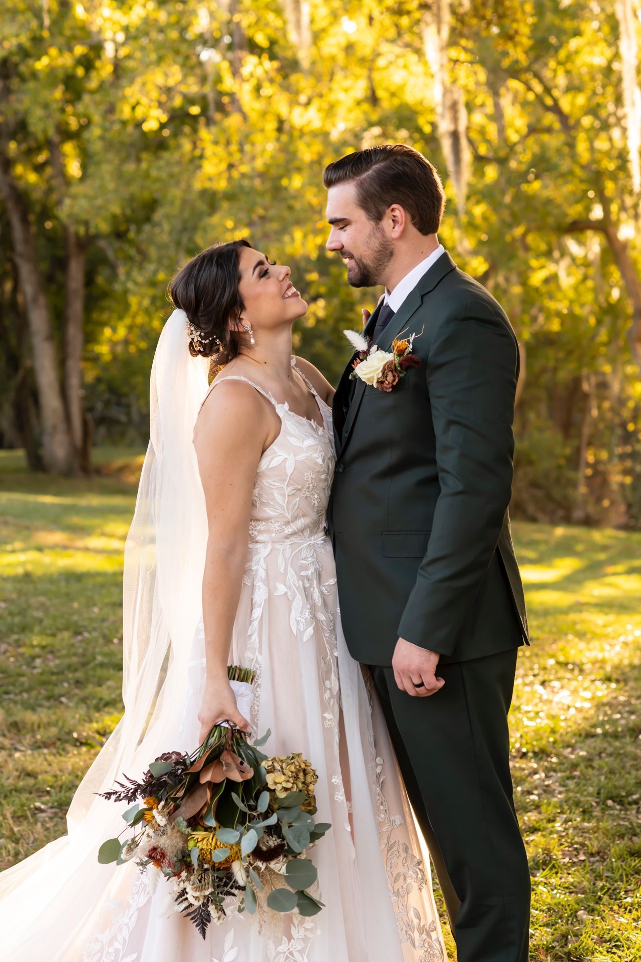 Newlyweds share romantic moments in golden autumn sunlight beneath trees during outdoor wedding photos.