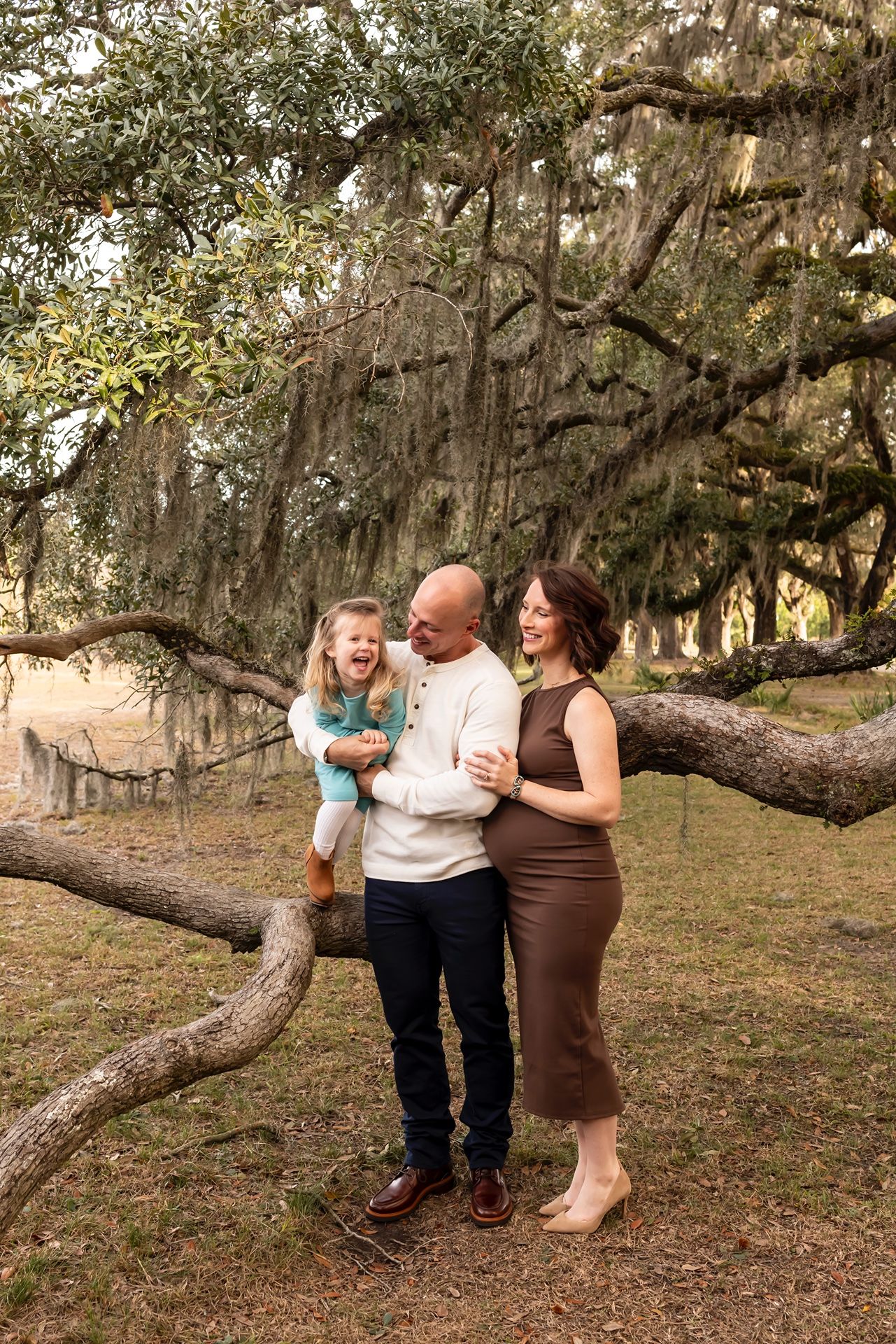 Family enjoys a tender moment together under Spanish moss draped trees in a natural outdoor setting.